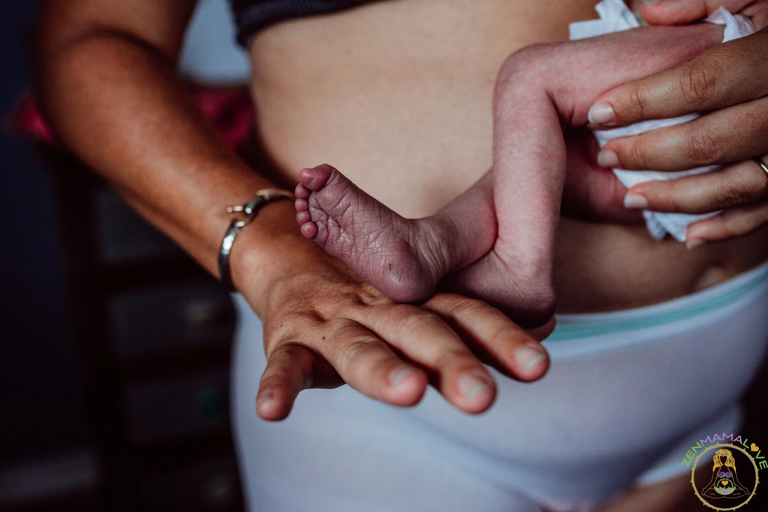 Close-up of a tiny, curled infant finger gently grasped by adult hands.