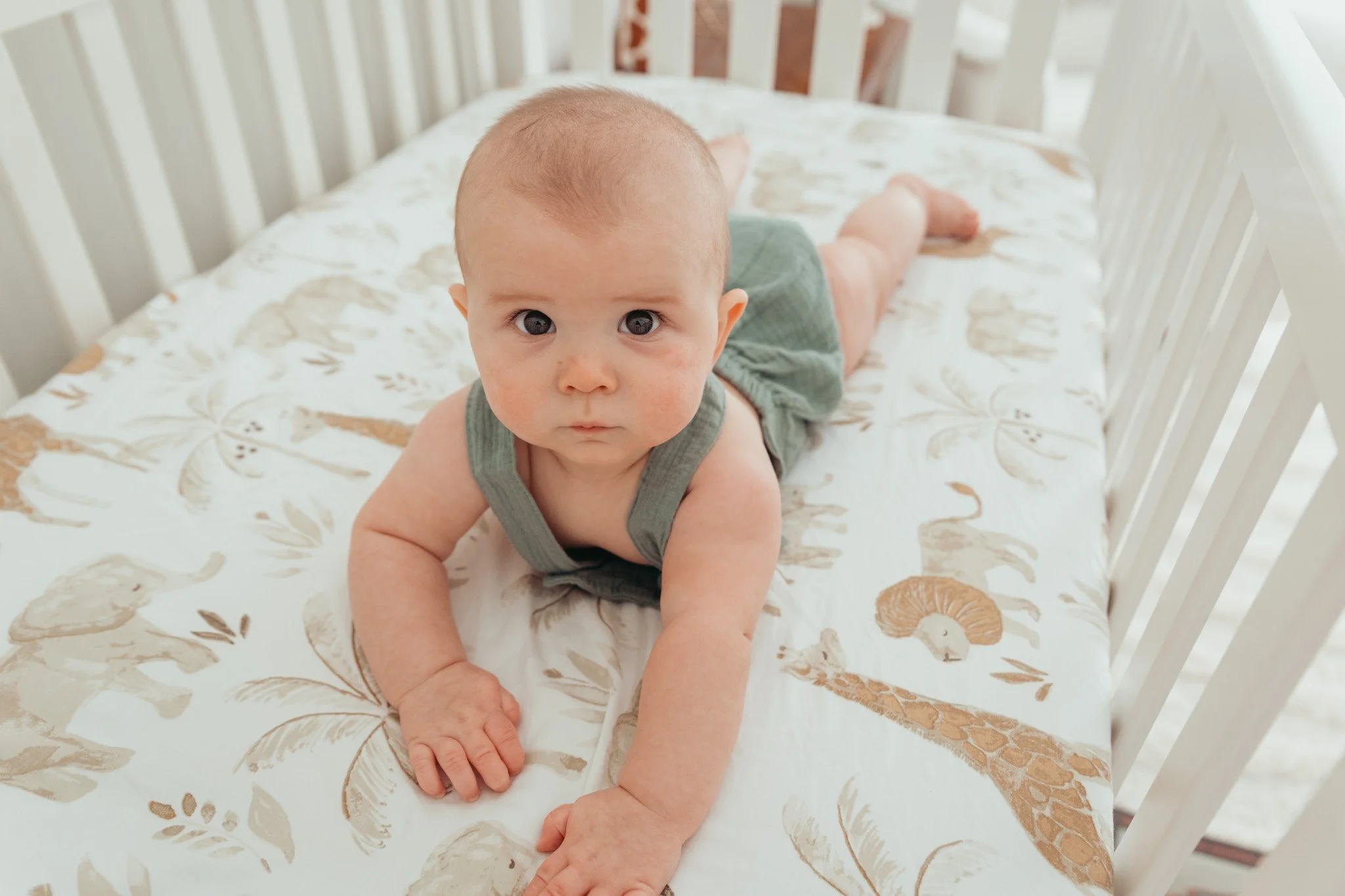 A baby crawling on a crib mattress with a painted floral pattern.