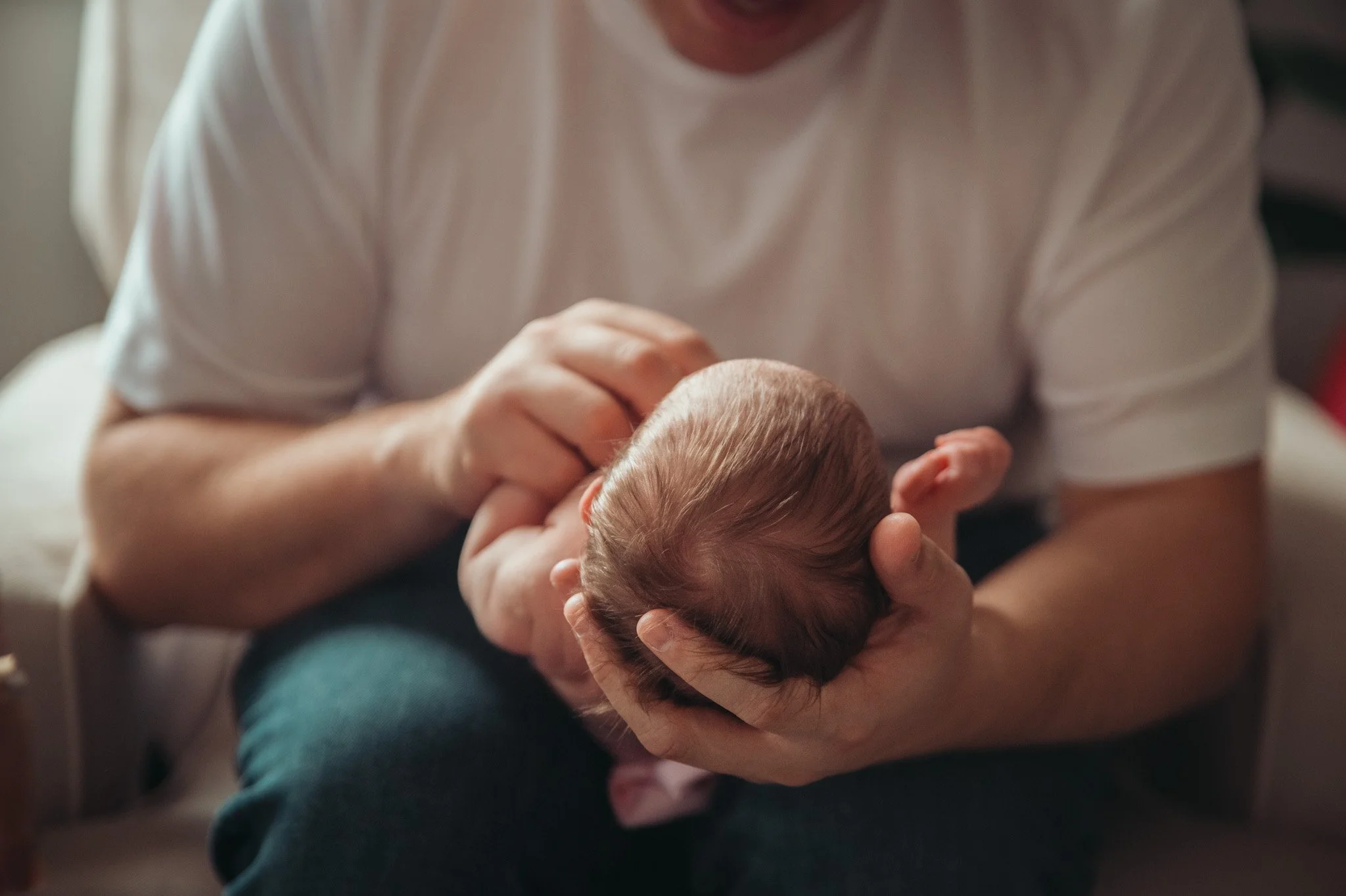 Close-up of a person holding a baby's head, gently supporting it with their hands.