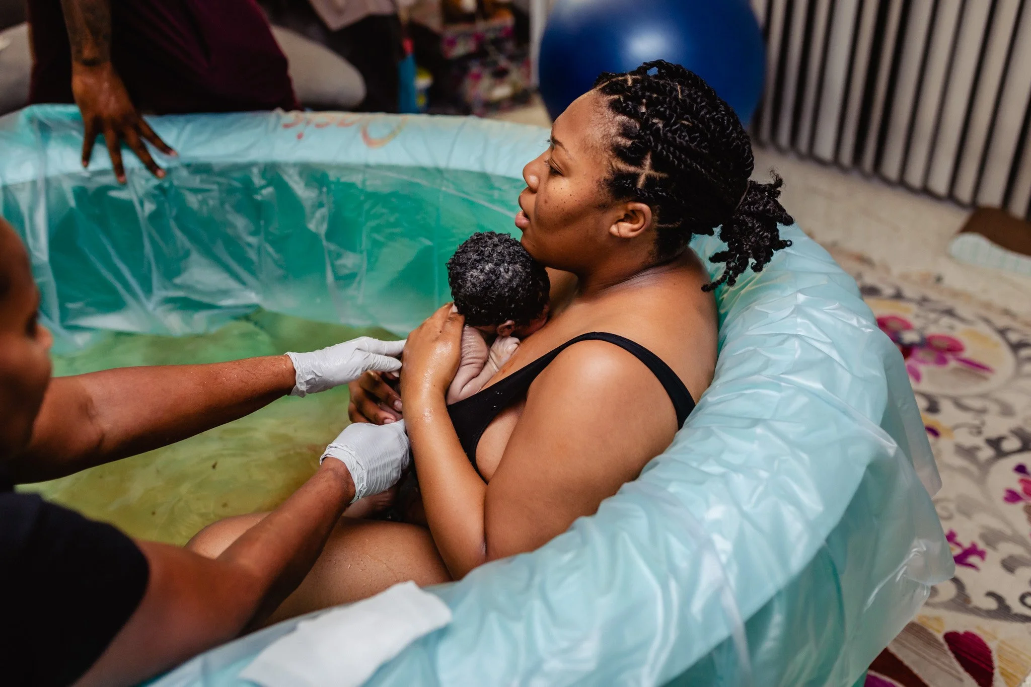 A woman giving birth in a birthing pool, with medical staff assisting. The woman is holding her newborn baby.