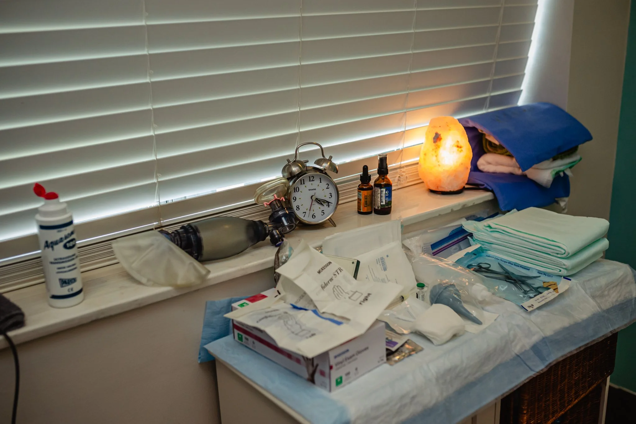 Medical supplies on a cluttered counter, including an alarm clock, bottles, tissues, and various medical packaging.