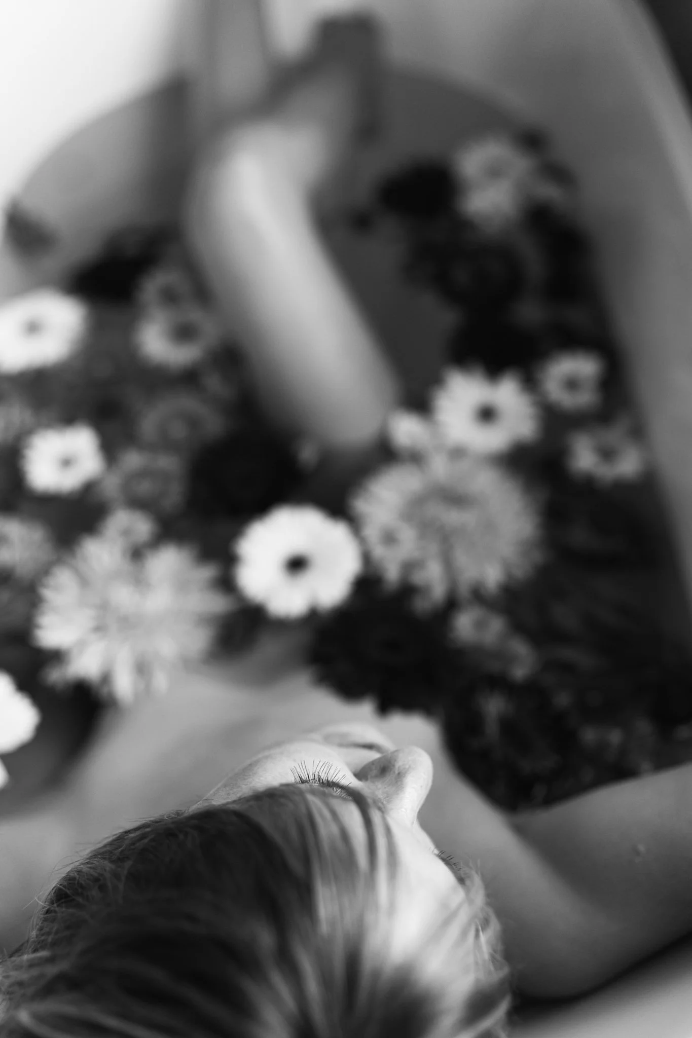 A person holding a cup of coffee, with a display of flowers behind them, captured in black and white.