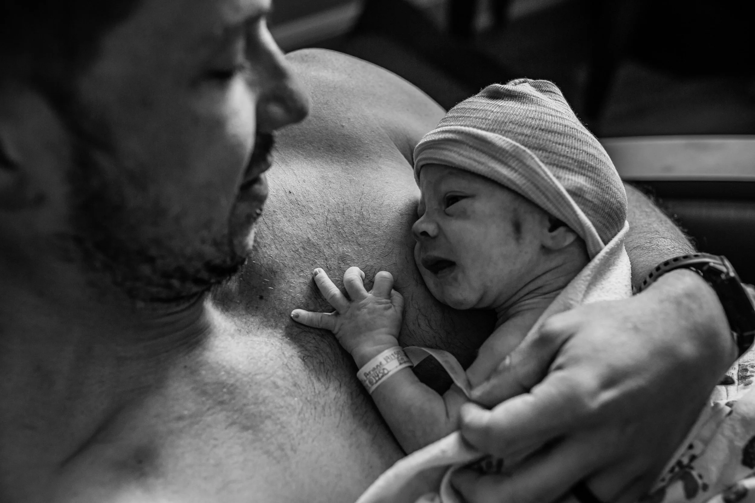 A newborn baby in a hospital, breastfeeding while lying on a person's chest, with a hospital wristband visible