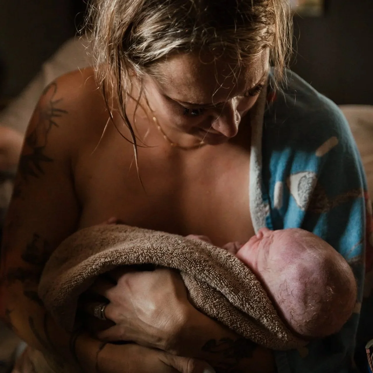 A woman with tattoos holding an newborn baby wrapped in a towel.