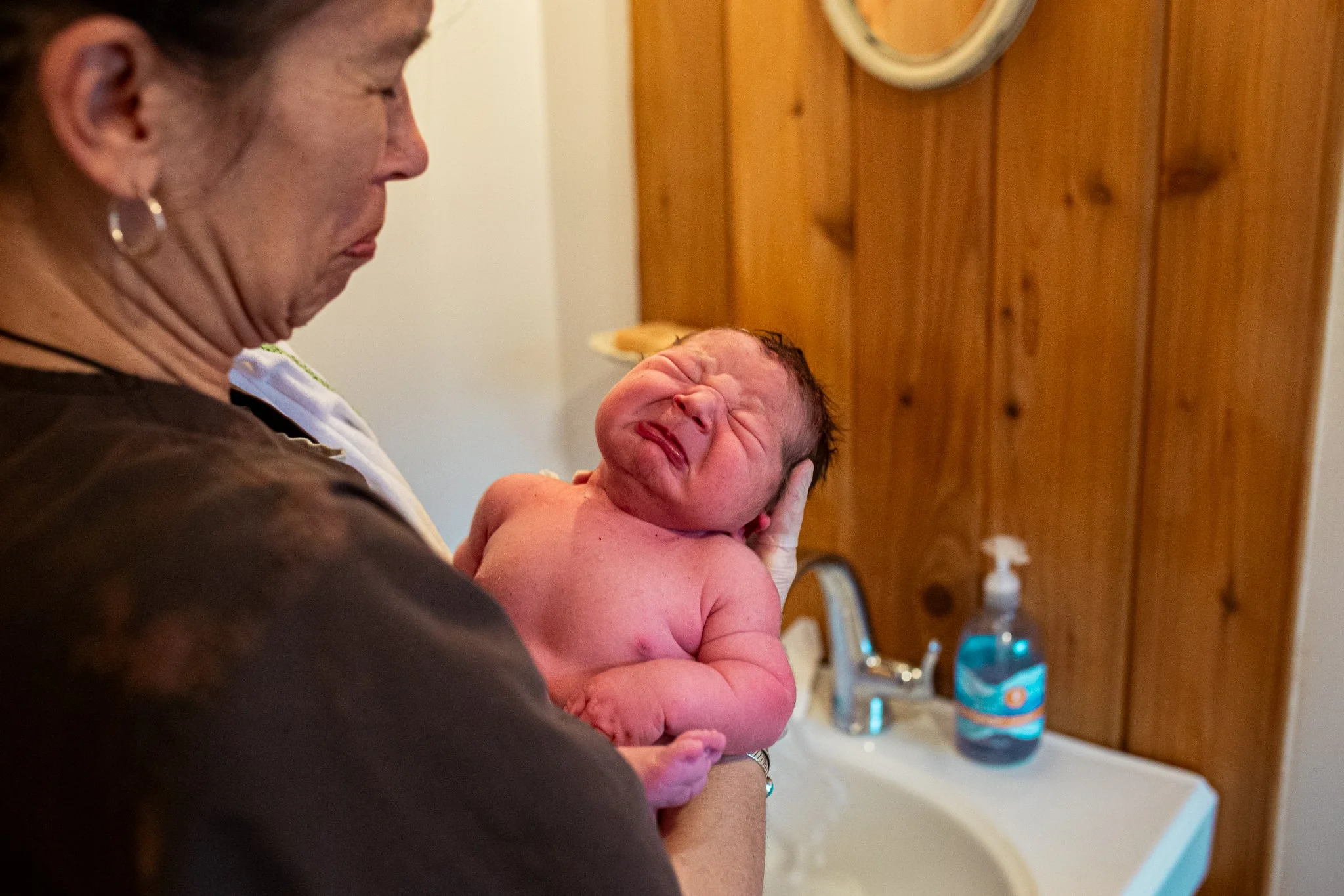 A woman holding a crying newborn baby in a room with wooden walls.
