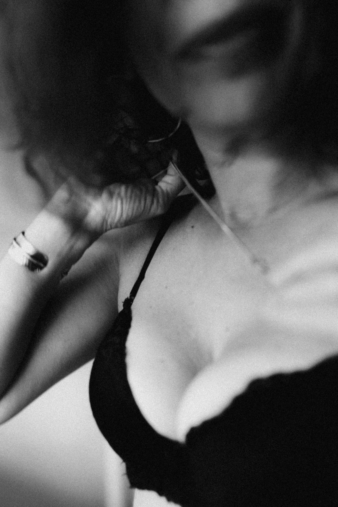 Close-up black-and-white photograph of a person's arm with a visible tattoo, holding a handgun, with part of the person's face and neck blurred in the background.