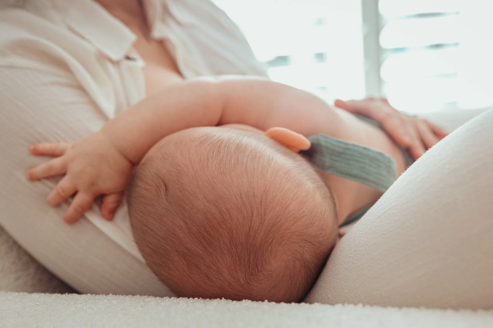 Close-up of a baby's head and hand resting on an adult's arm, with soft lighting.