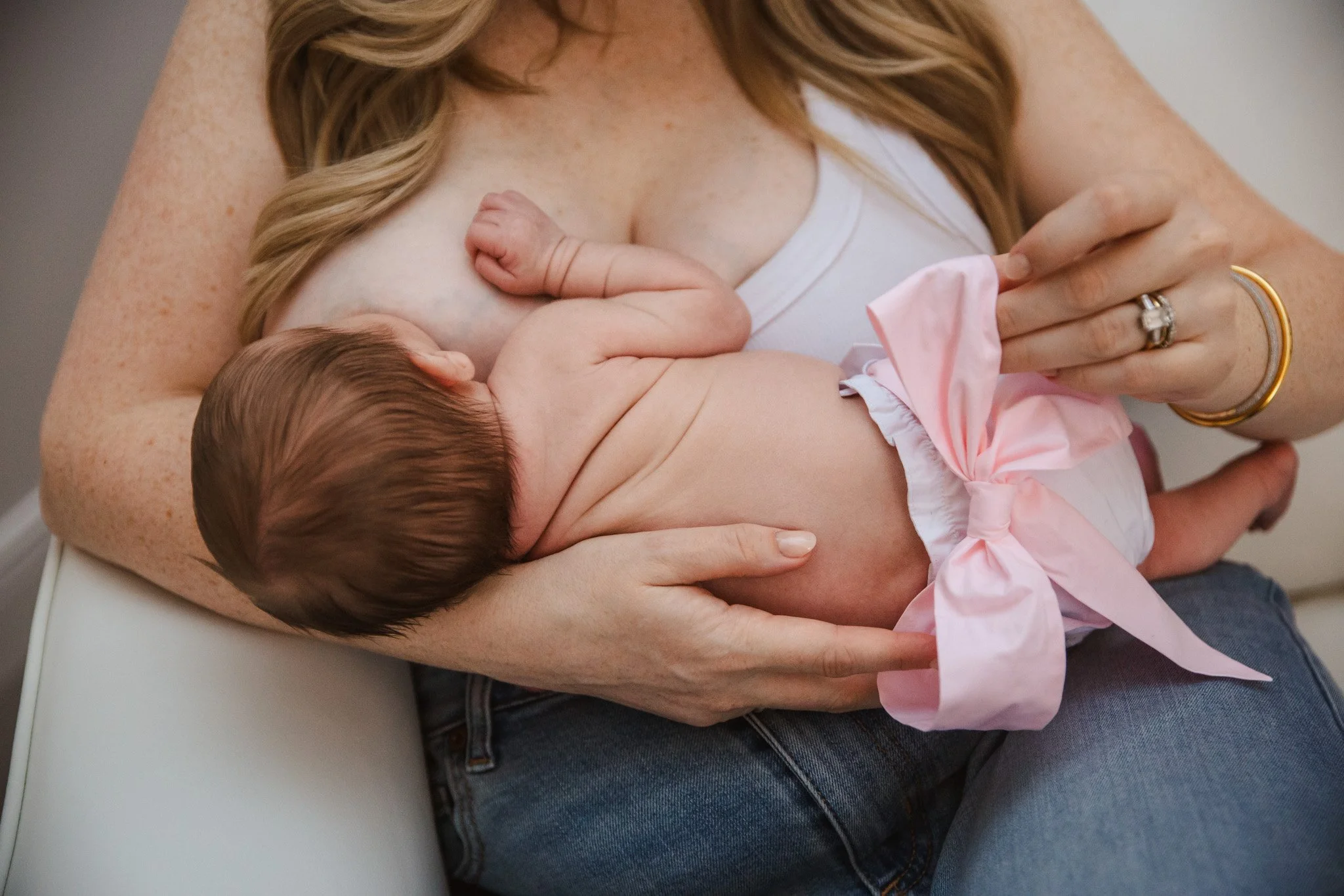 A woman with red hair holding a baby in a white shirt with pink accents, breastfeeding.
