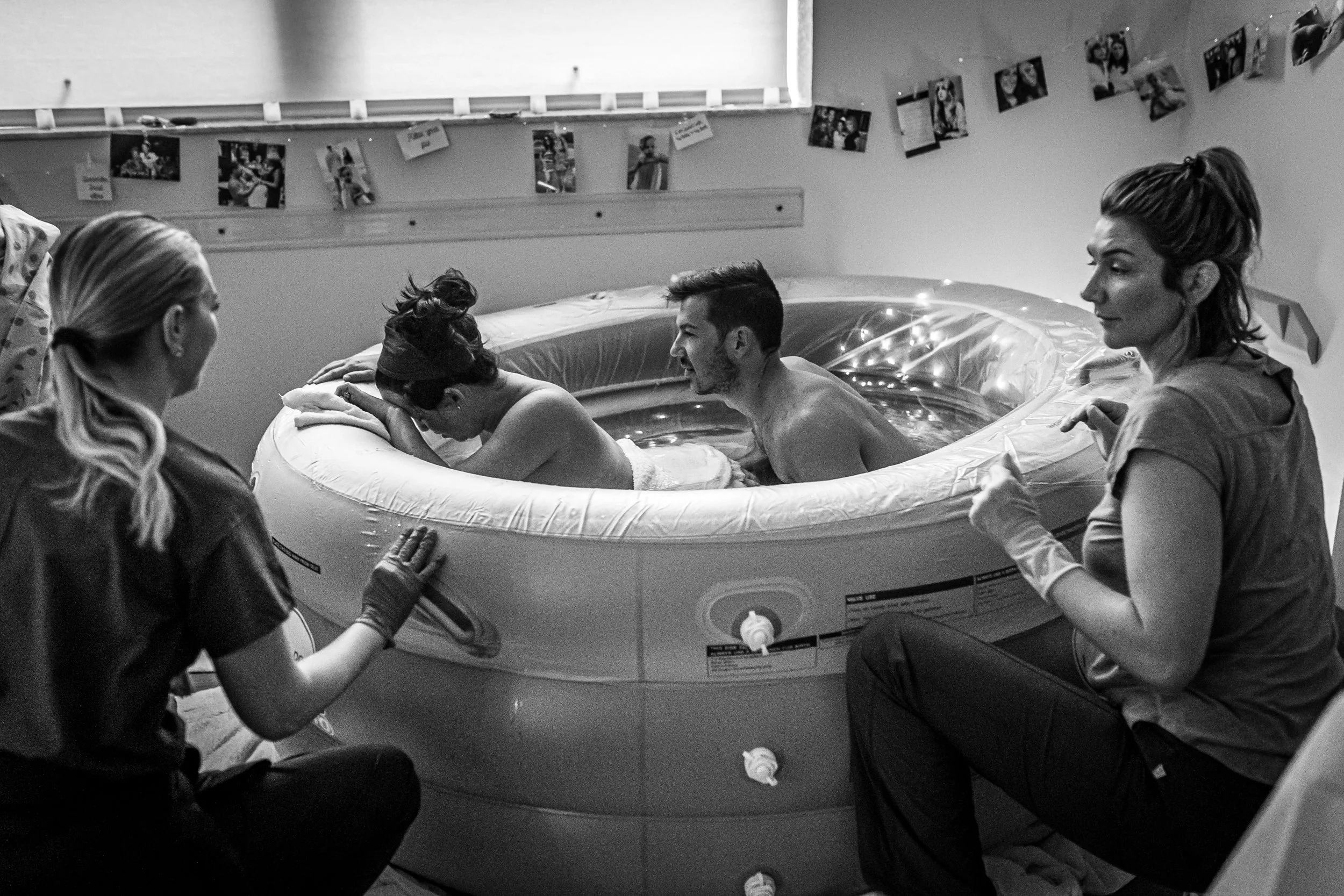 Five people gathered around an inflatable hot tub, with two women and three men, one with short hair laughing, another with hair tied back, and an older woman with long hair. The woman with long hair has her hand on the side of the tub, and one of th