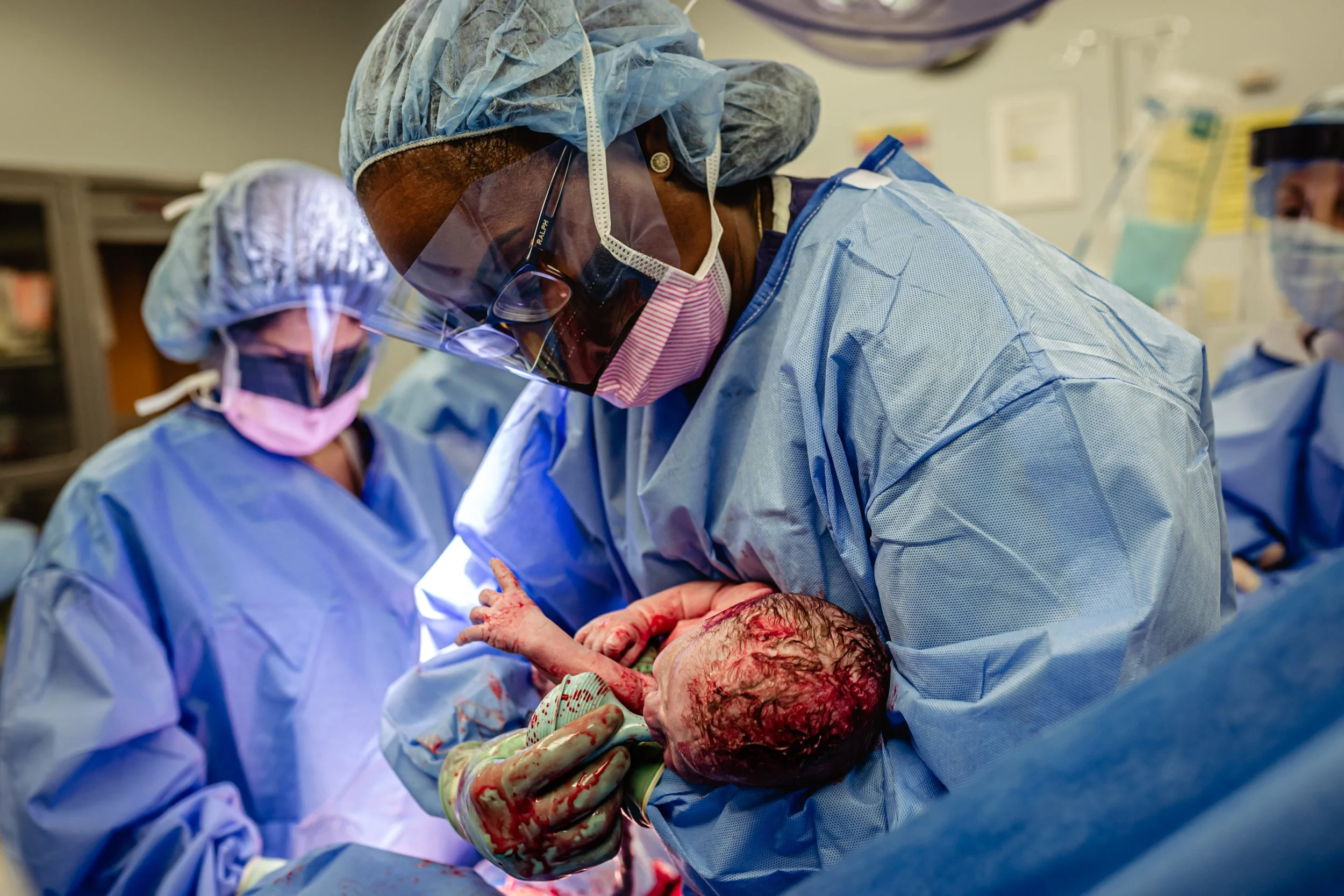 Medical team performing surgery on a newborn baby in an operating room, with the medical professional holding the baby carefully.