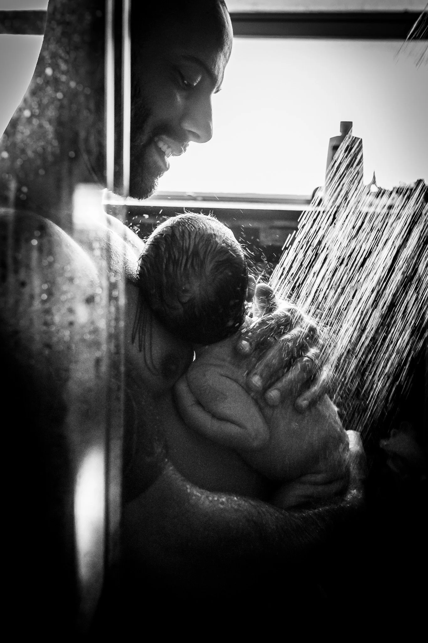 A man holding and comforting a crying baby in the shower.