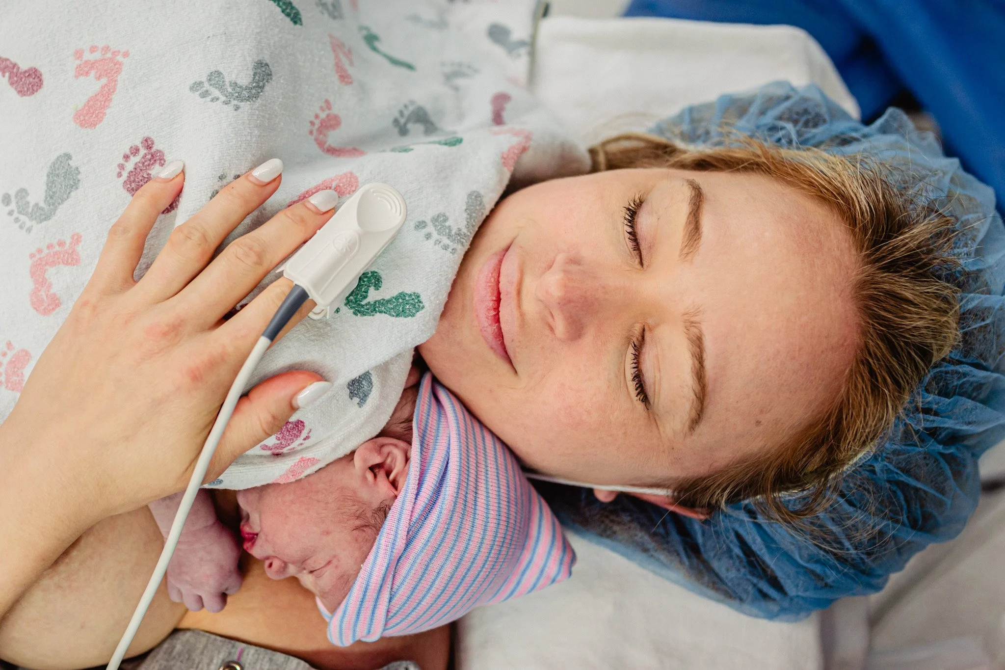 A woman with closed eyes holding a newborn baby close to her chest, both lying in bed.