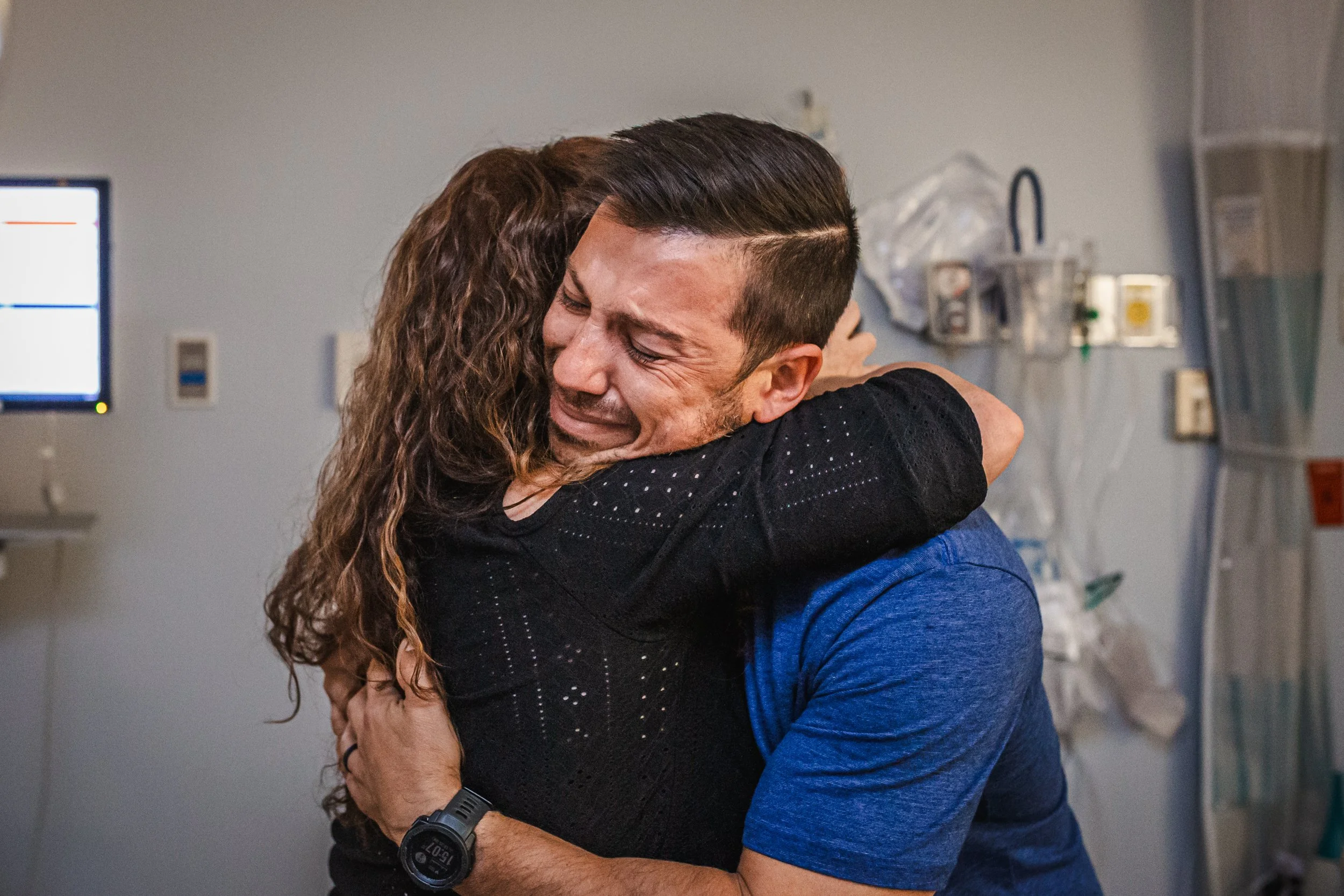 A man and woman are hugging each other warmly in a hospital room, showing joy and emotional connection.