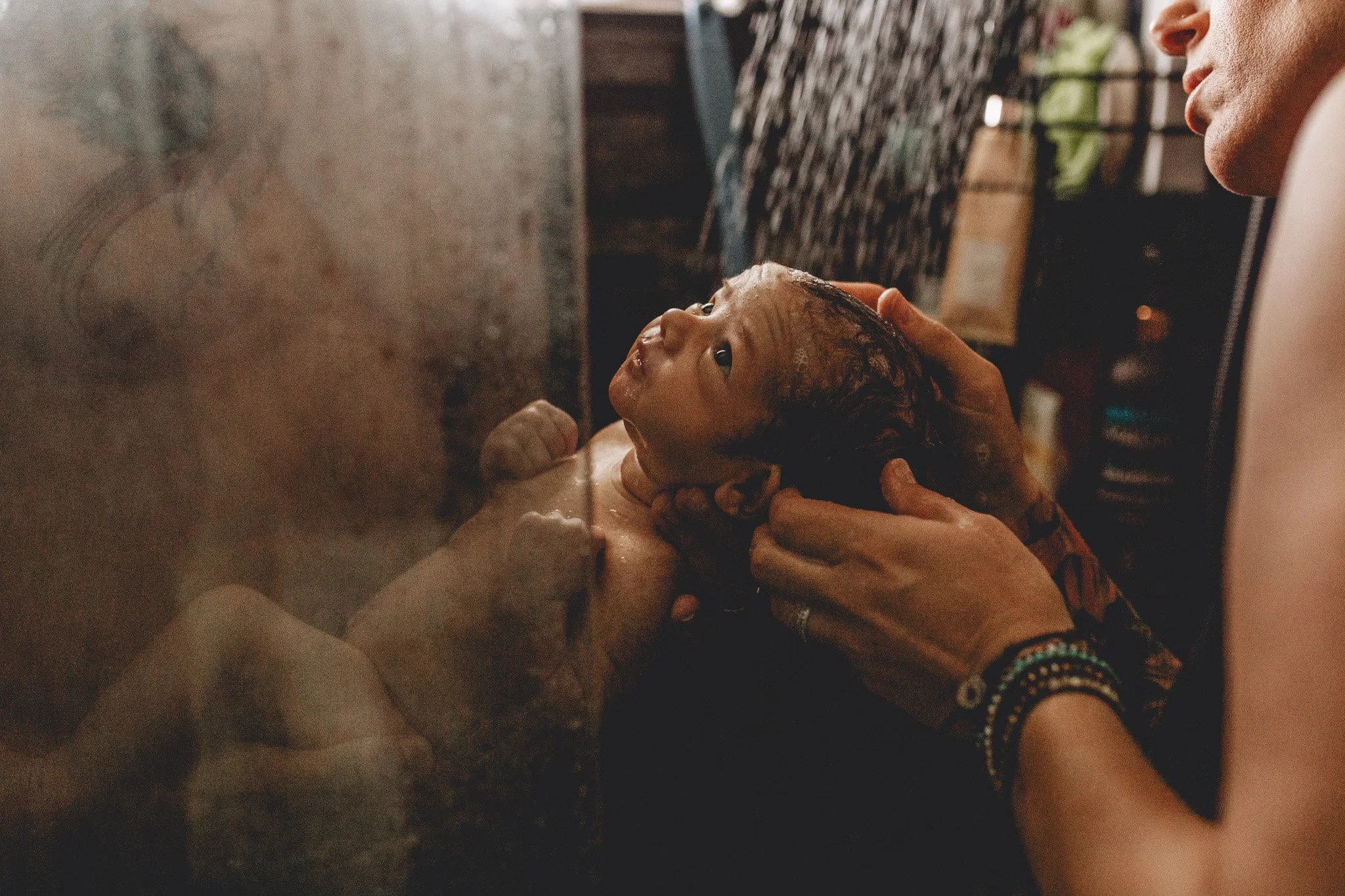 A woman helping a newborn baby during a water birth, with the baby's head and shoulders visible and the woman holding the baby gently.