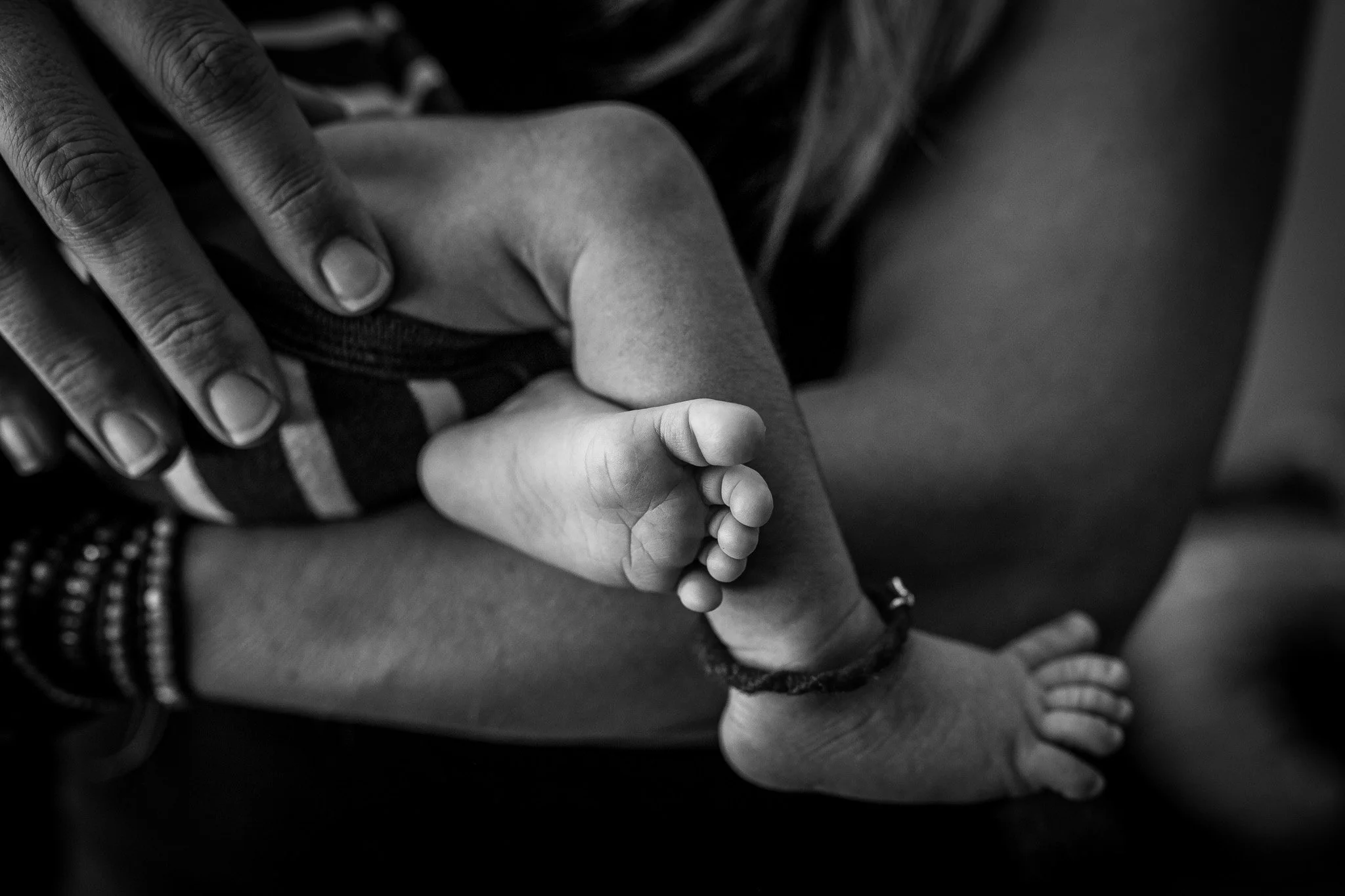 Close-up of an adult hand gently holding a child's hand, both hands are in black and white, with some visible accessories on the adult's wrists.