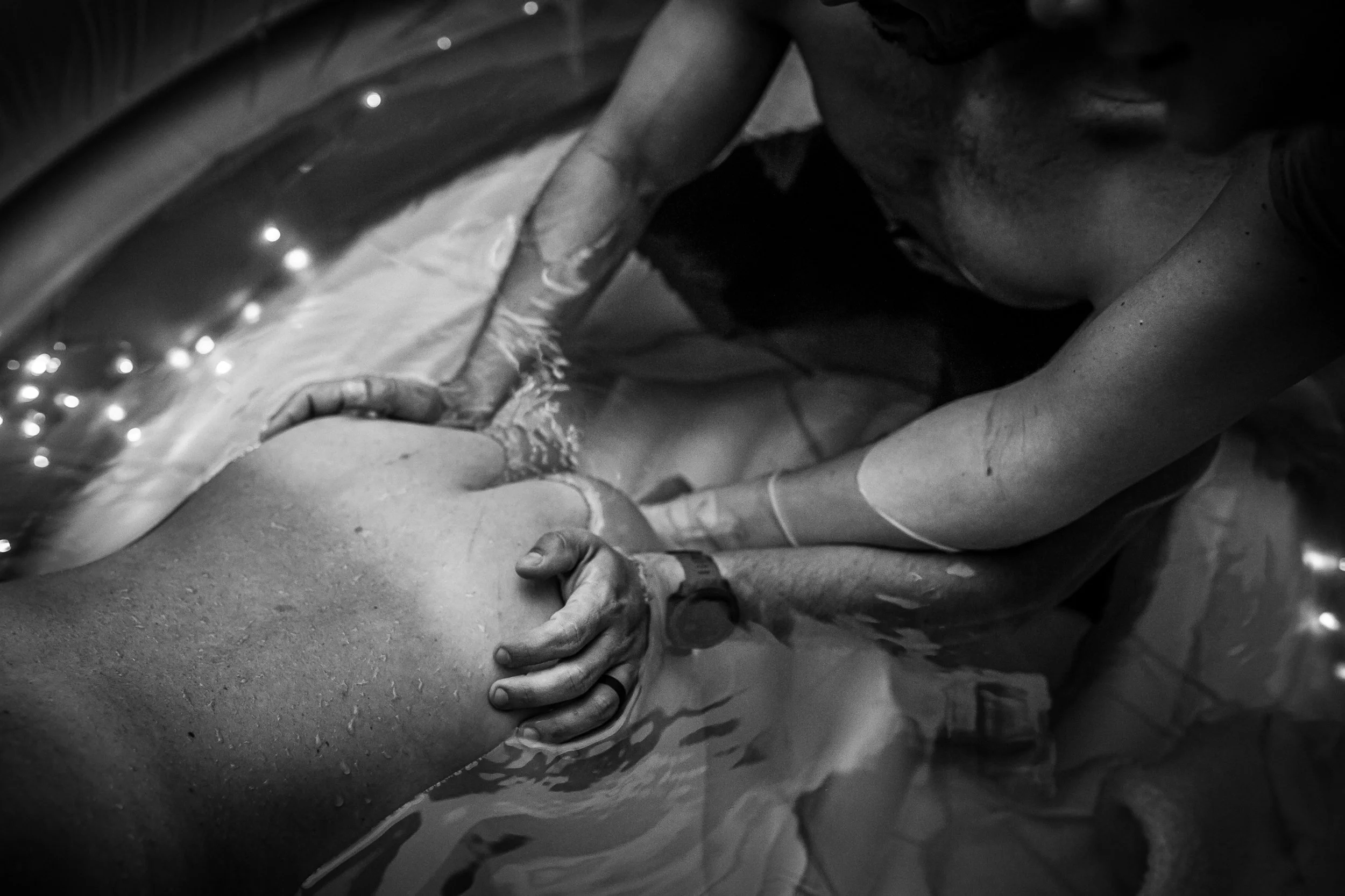 A person lying on a surface with another person's hands on their back, with water droplets on the surface and hands, indicating a massage or physical therapy setting.