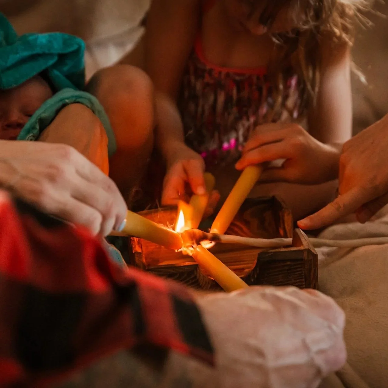 People lighting candles in a dimly lit setting, possibly a religious or spiritual ritual.