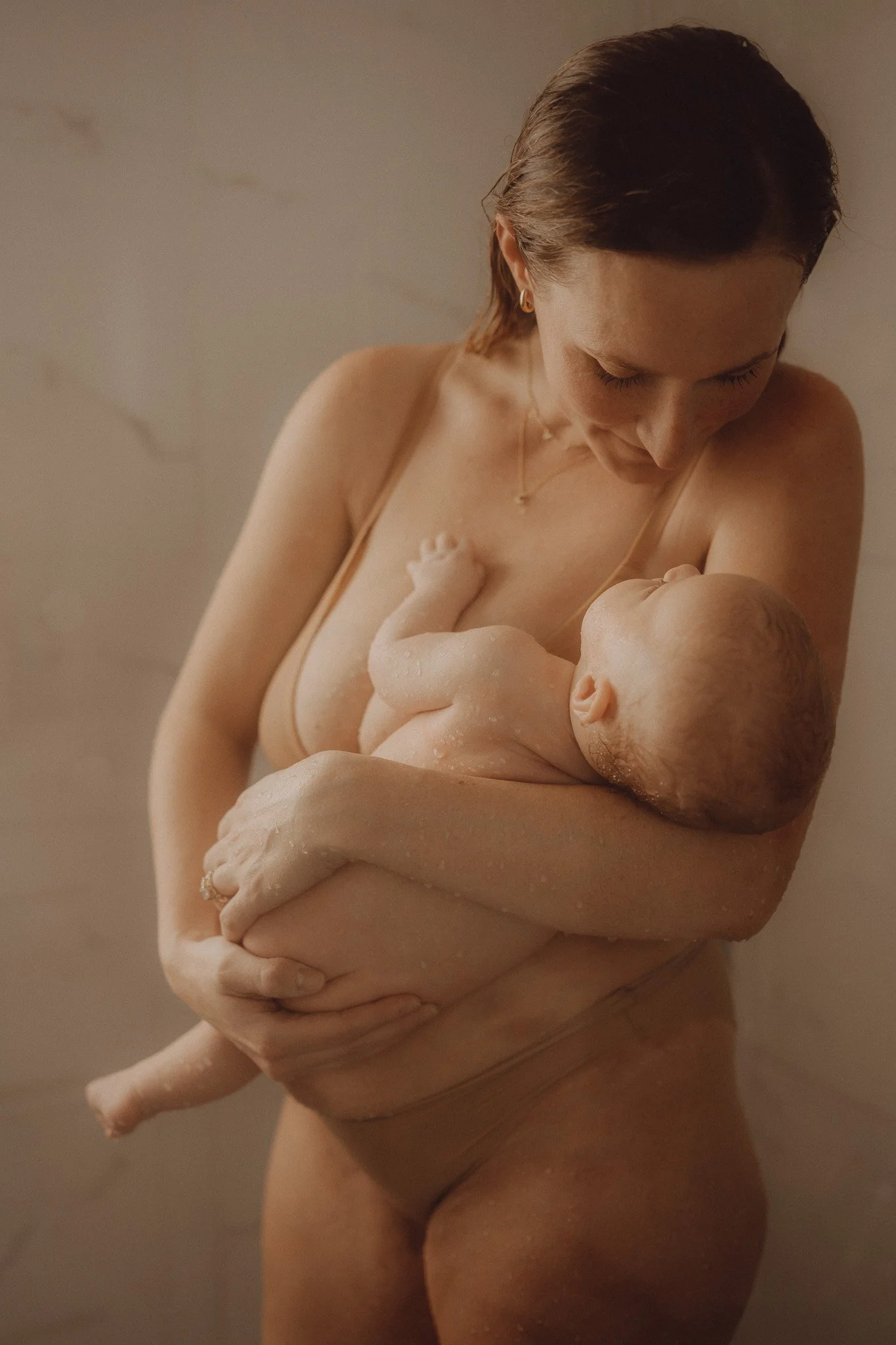 A woman holding a newborn baby in a warm, intimate moment, with a neutral background and soft lighting.