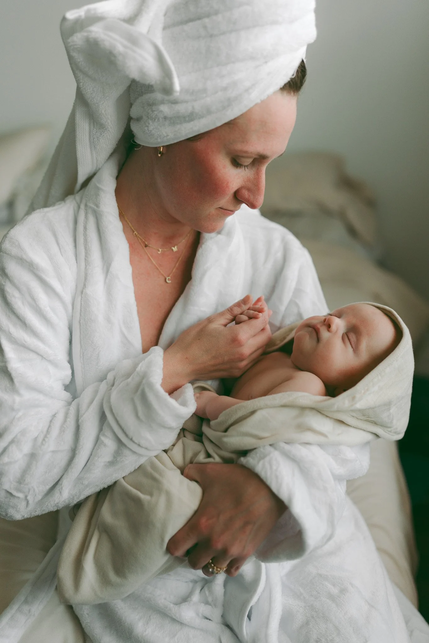 A woman wearing a white towel on her head and jewelry holding a sleeping baby wrapped in a blanket.