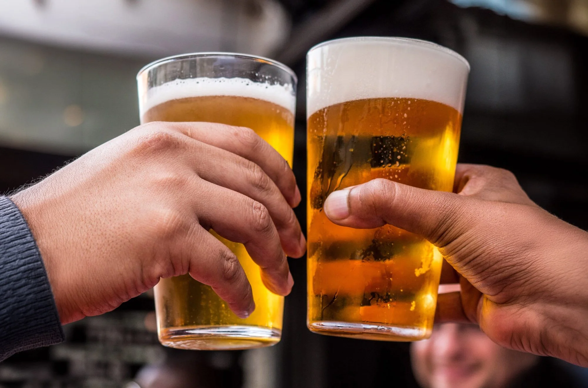 Two people holding glasses of beer for a toast.