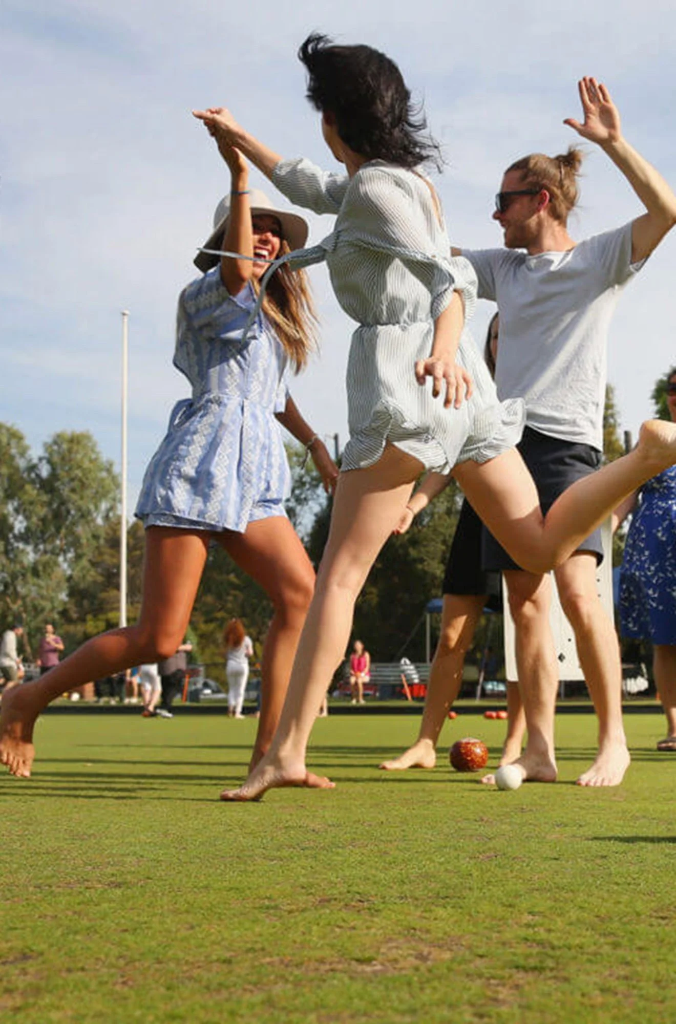 Group of people playing croquet on a grassy field on a sunny day.