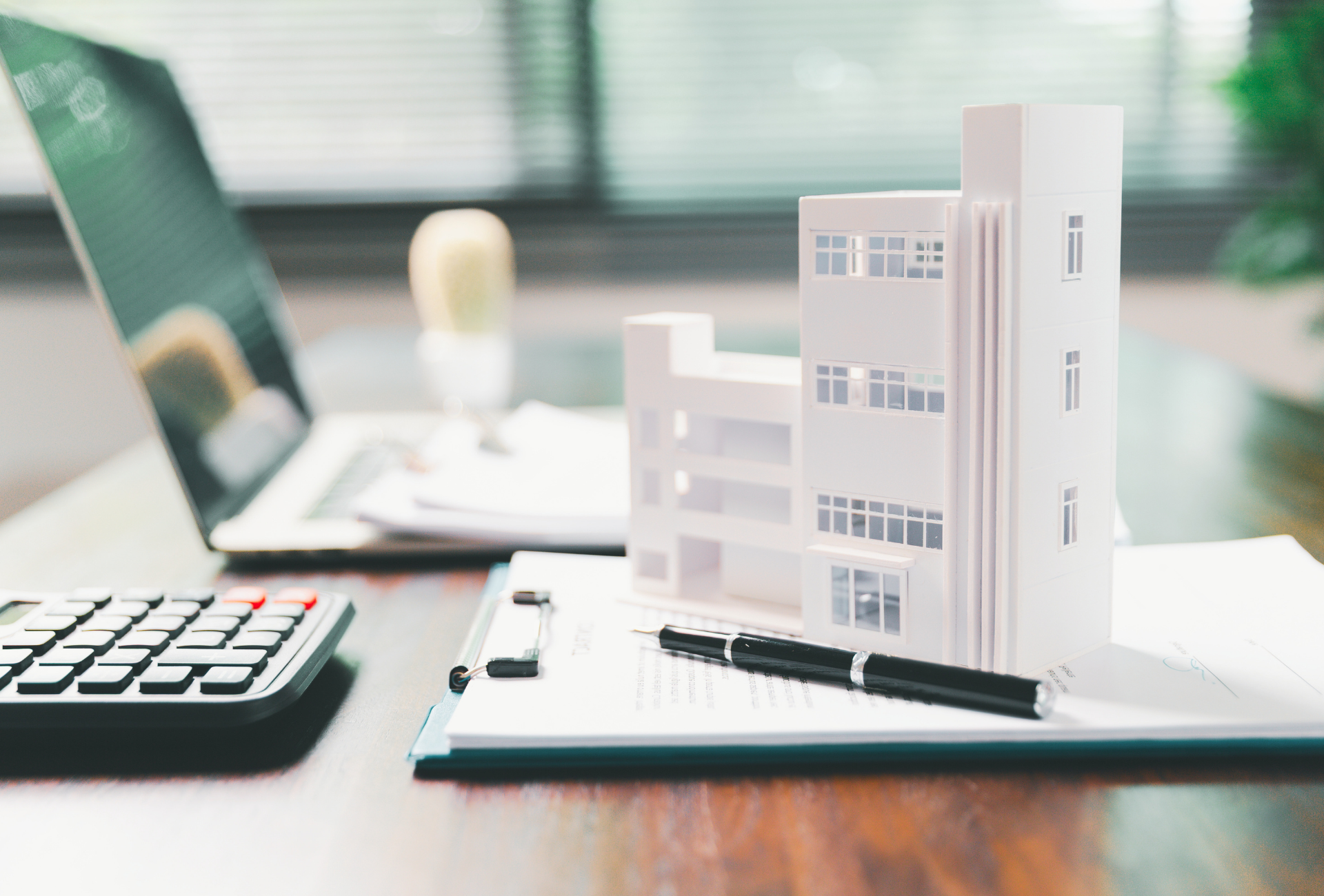 A white architectural model of a modern multi-story building with glass windows on a desk.