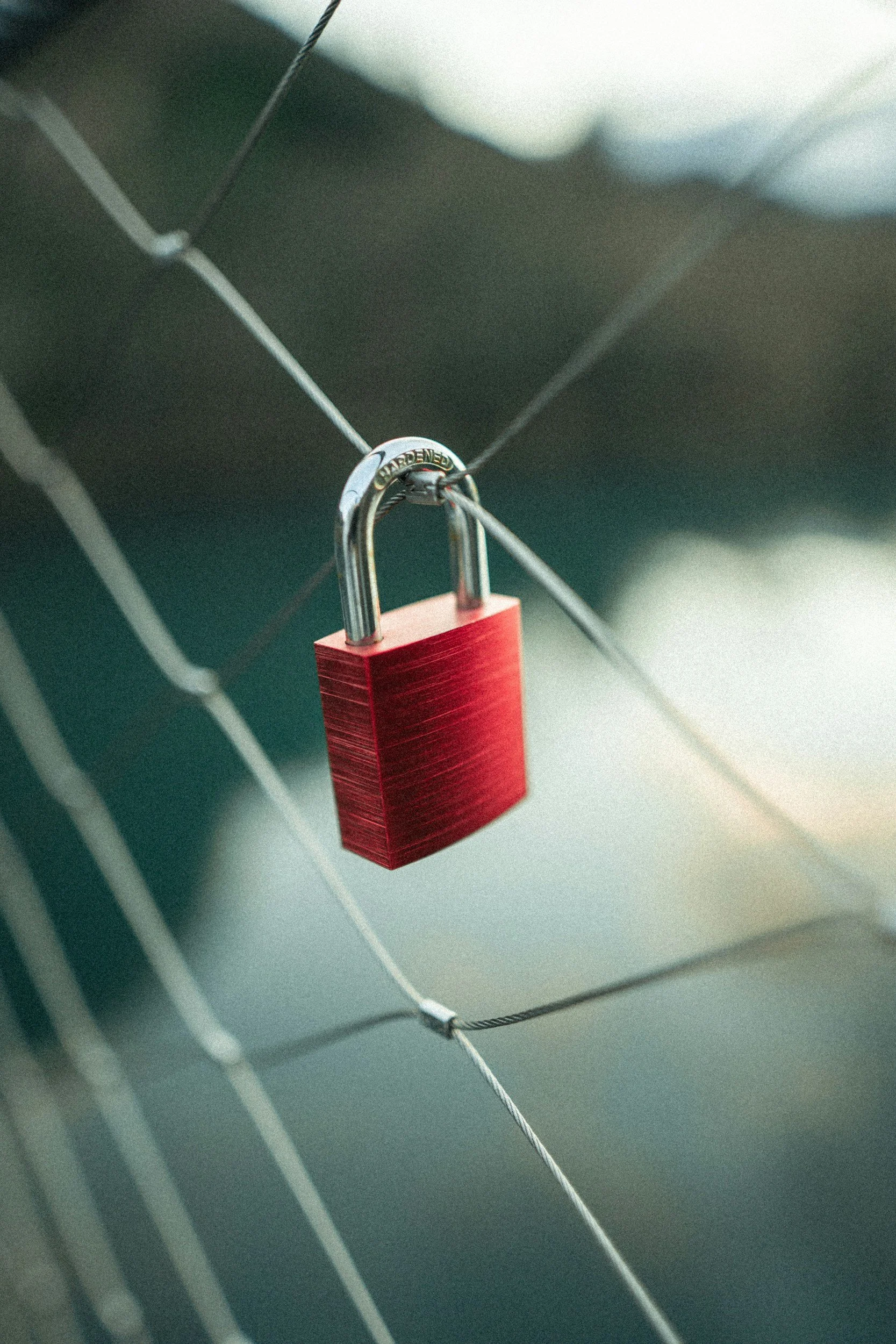 A red padlock securing two wires on a metal grid background.
