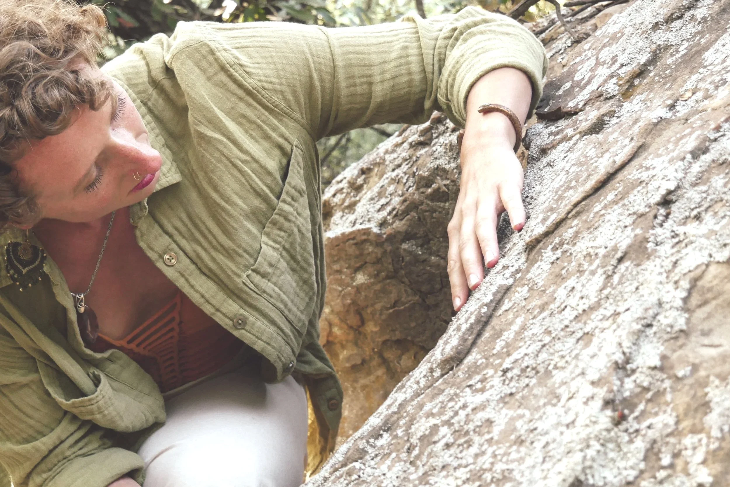 A woman with curly blonde hair and a septum piercing rock climbing on a rocky surface outdoors.