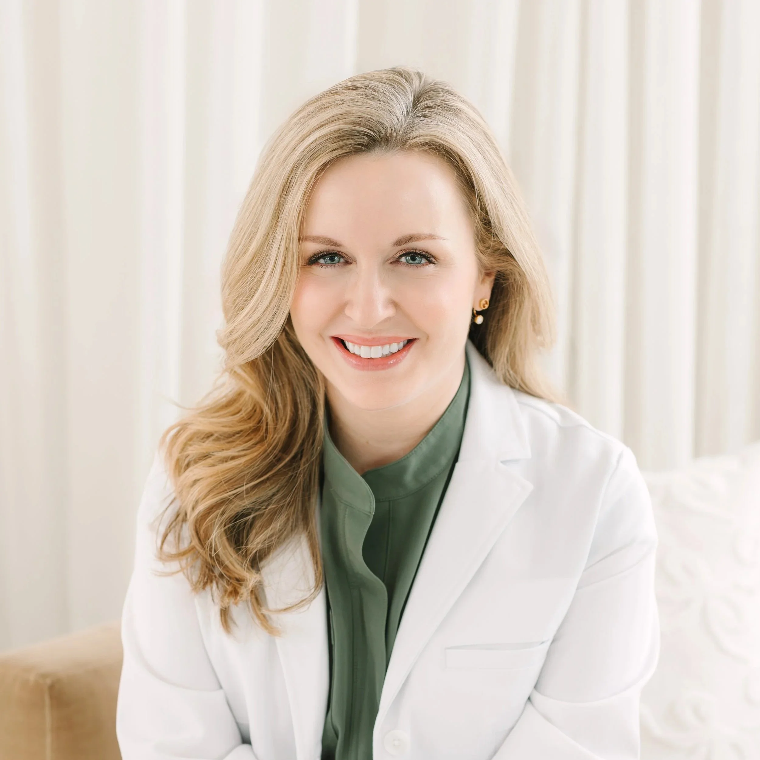 Dr. Lesley Starnes with blonde hair wearing a white coat, green shirt, and pearl earrings, smiling with a neutral background.