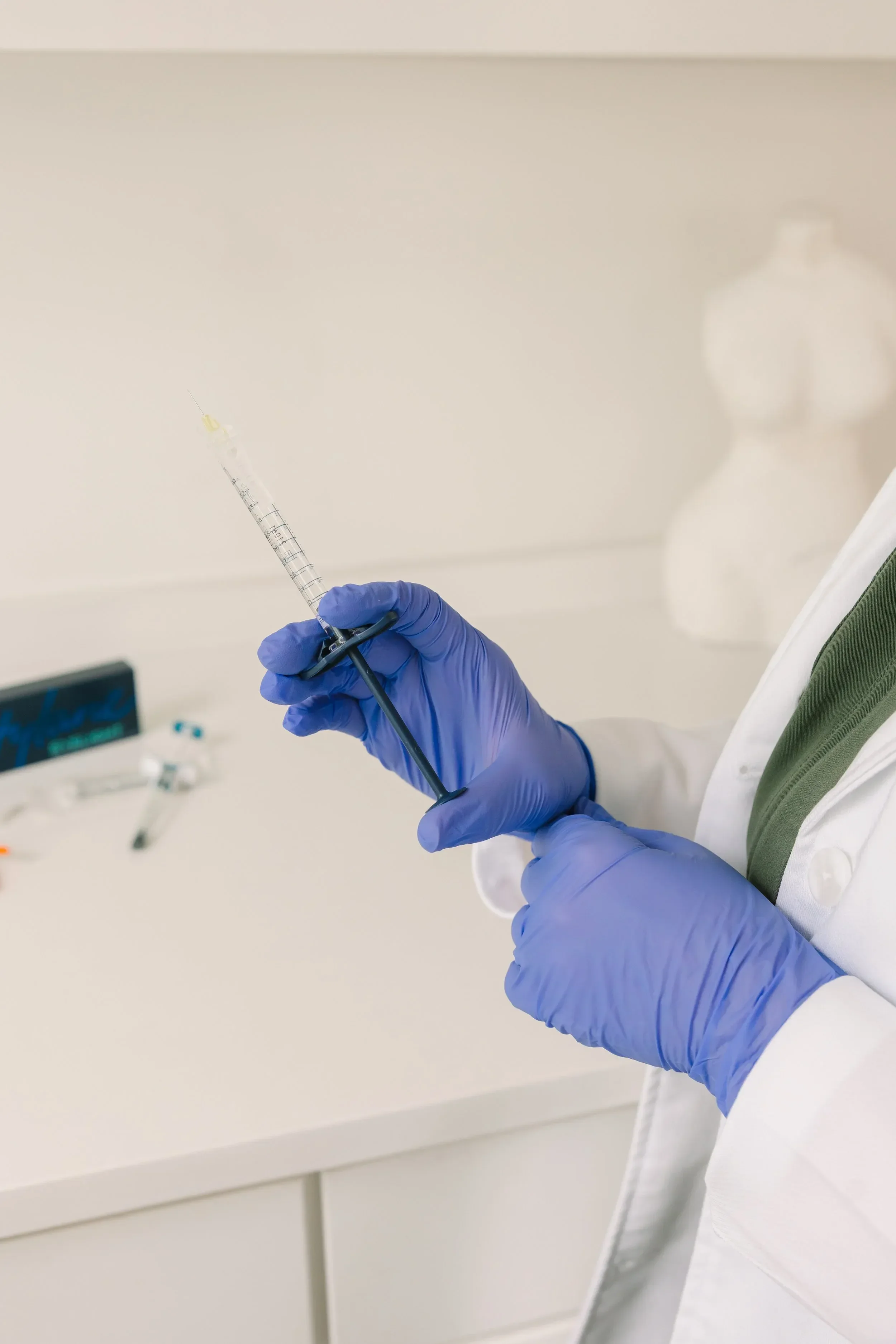 Close-up of a medical professional wearing blue gloves holding a syringe with a needle, preparing to administer an injection in a clinical setting.