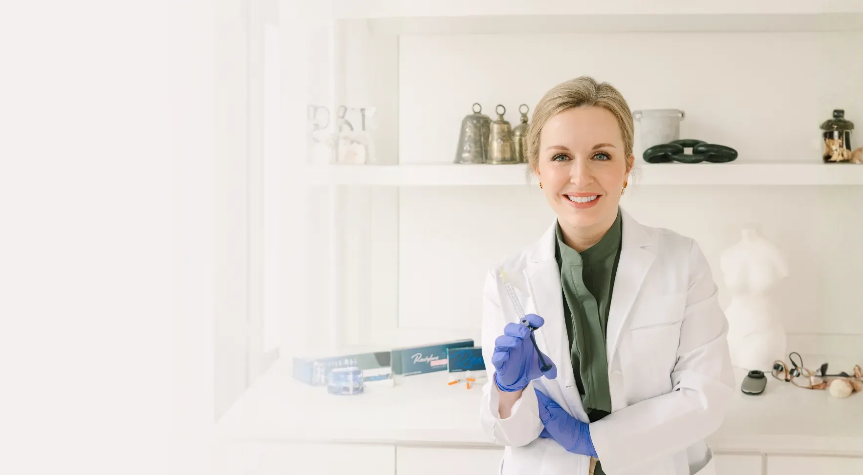 Dr. Lesley Starnes smiling in a white coat holding a syringe in a bright, modern medical office.