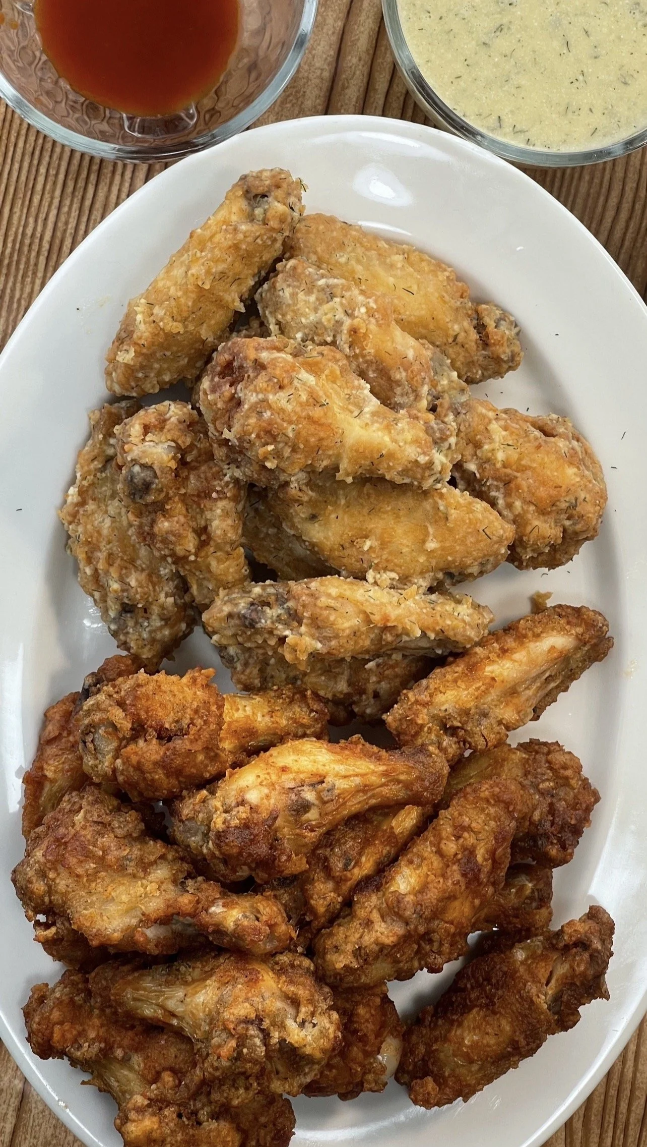 Basket of fried chicken pieces served on a white oval dish with two bowls of dipping sauces in the background.