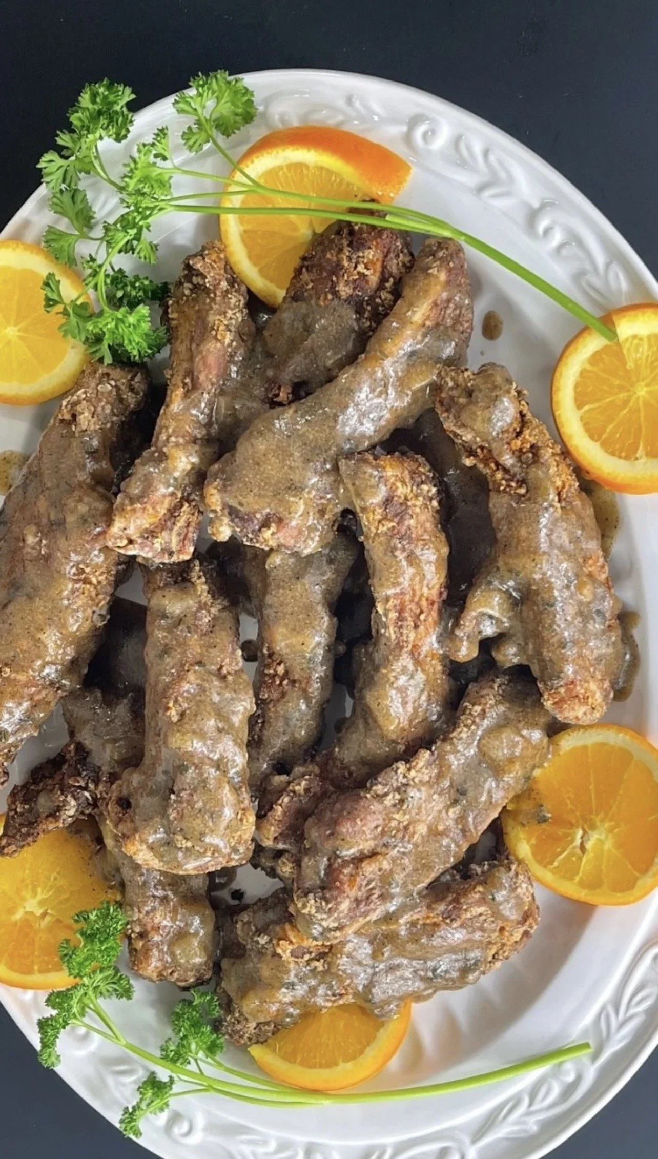 Plate of fried chicken wings garnished with orange slices and green herbs on a white platter.