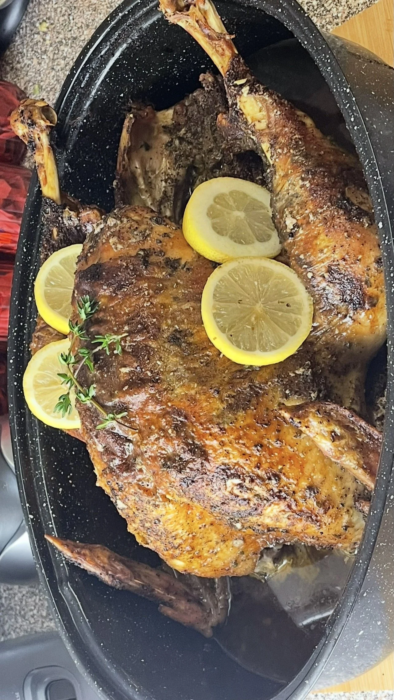 Baked whole turkey garnished with lemon slices and fresh herbs on a black platter.
