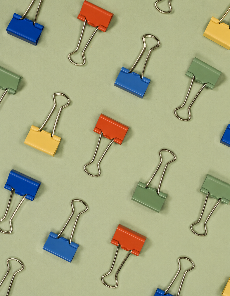 Assorted colorful binder clips scattered on a light green surface.