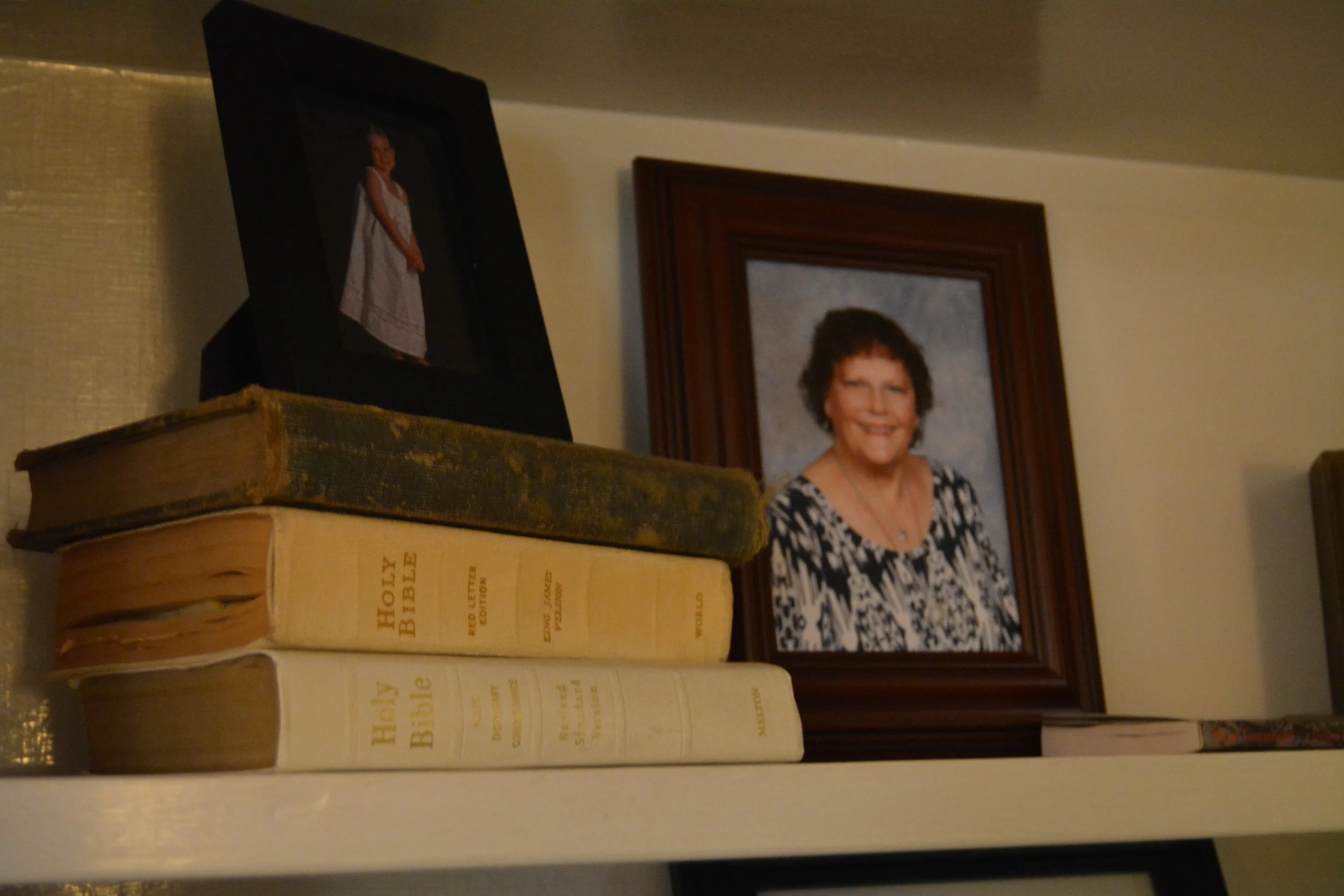 Photo of a woman smiling, framed in a wooden picture frame, placed above a large, old, thick Bible with a yellowed spine and cover.