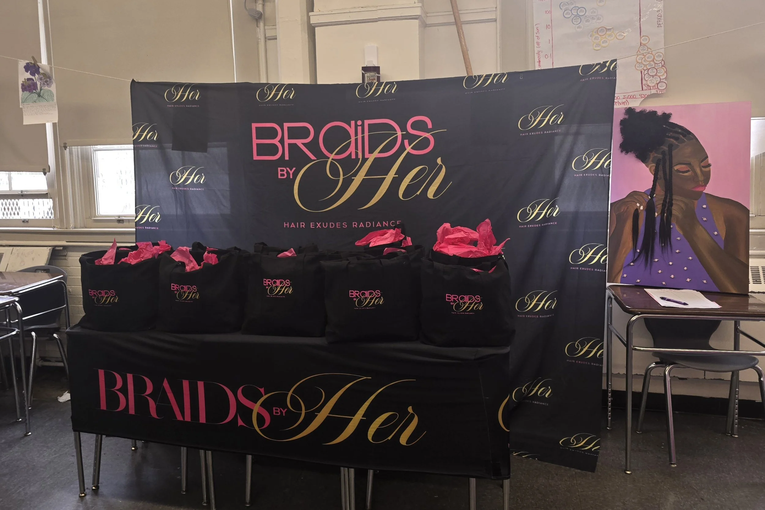 Display at a hair wig event reading 'Braids by Her' with black gift bags underneath, and a large painted portrait of a woman with braided hair, makeup, and jewelry on the right.