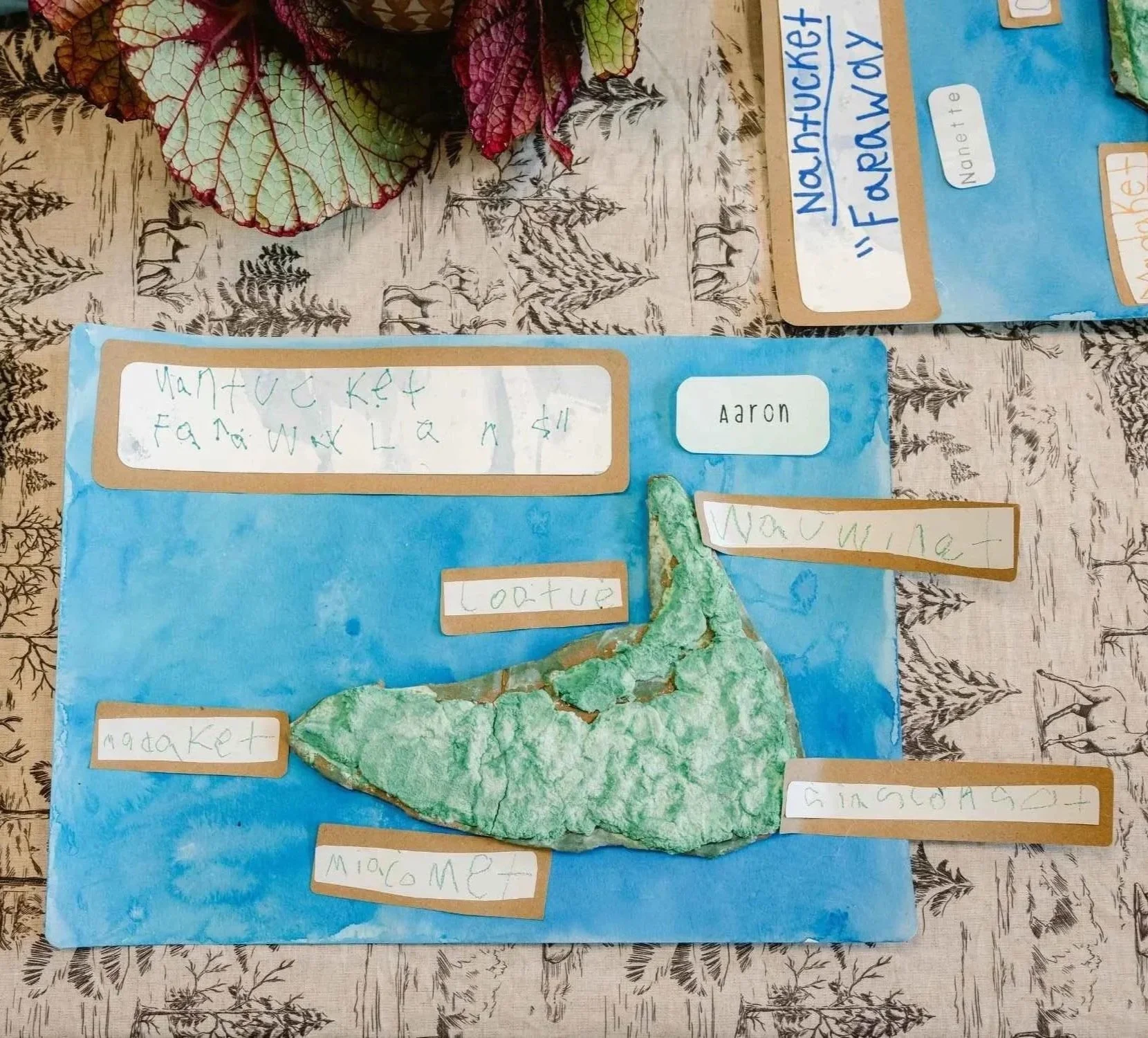 A Nantucket Lighthouse School student project displayed during Project Night, featuring a handmade map of Nantucket on blue paper with handwritten labels identifying different things.