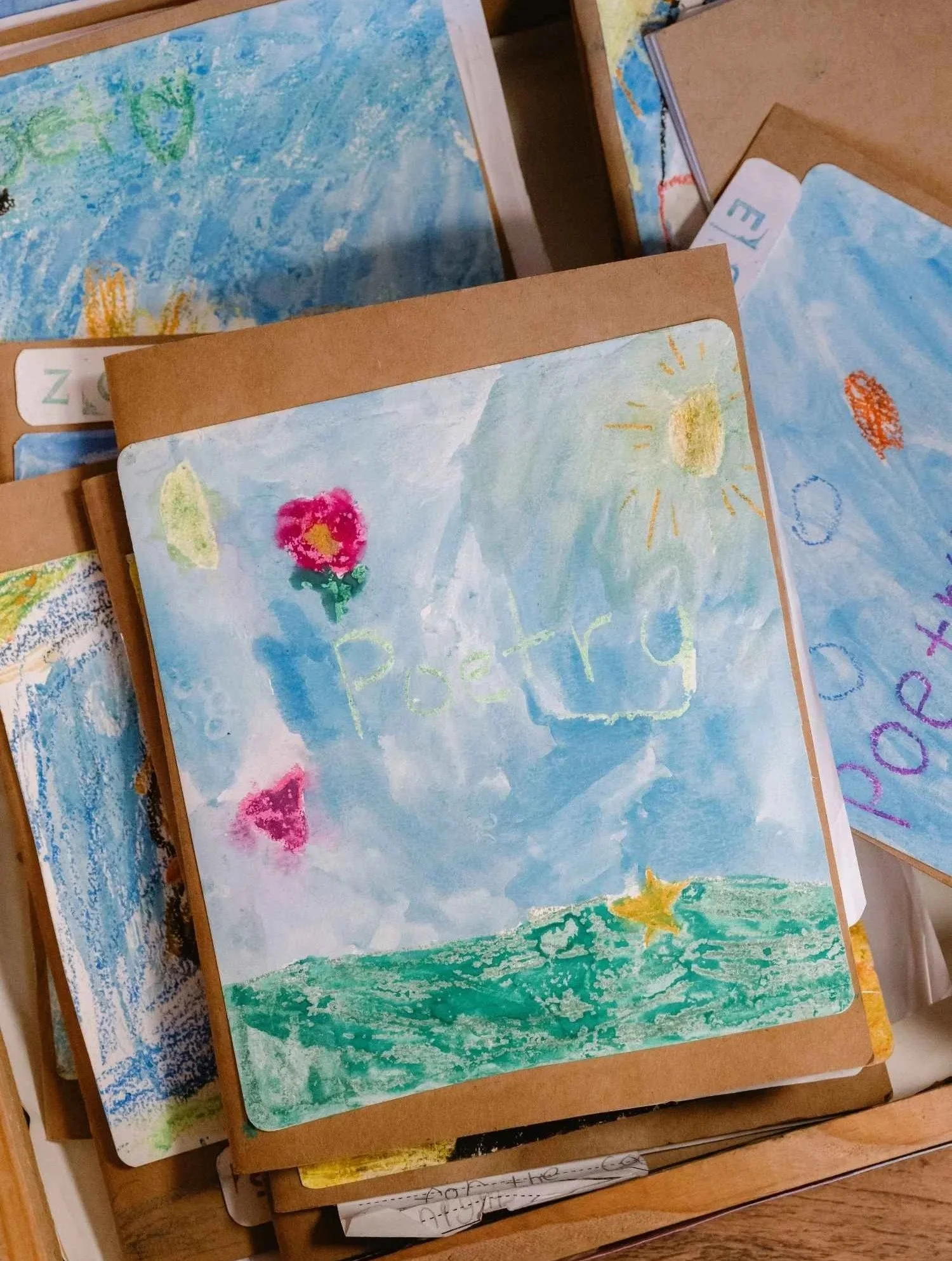 Poetry journals created by Nantucket Lighthouse School students displayed during Project Night, featuring colorful hand-drawn illustrated covers of the sun, sky, and natural world alongside their creative writing.