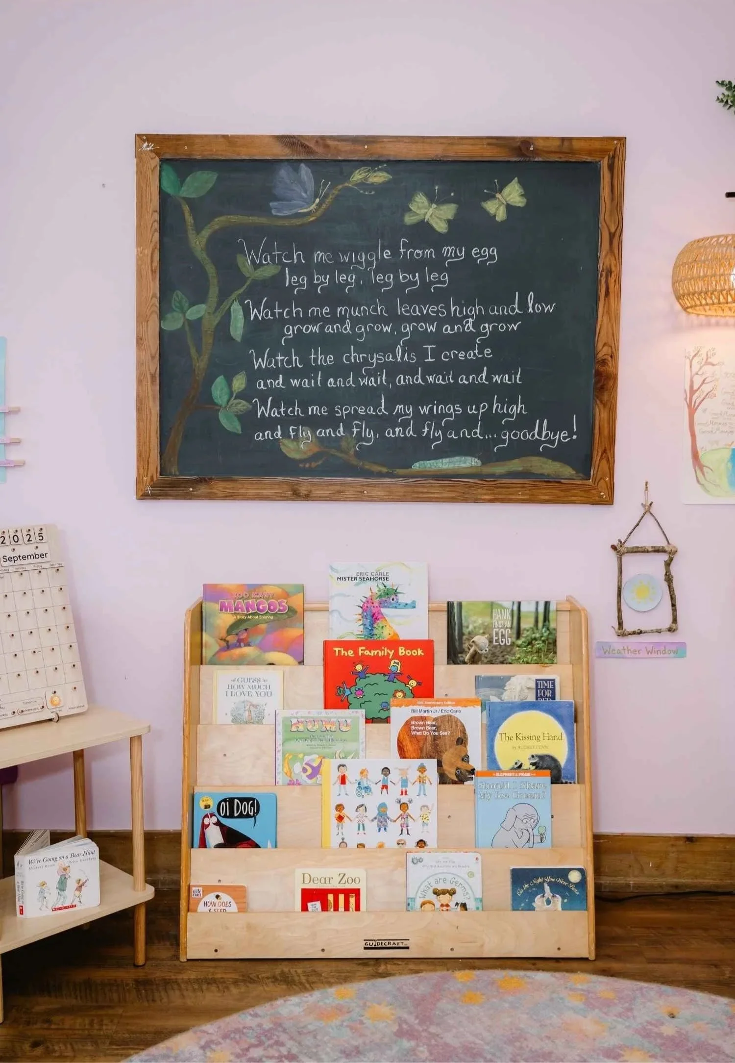 A Nantucket Lighthouse School classroom bookshelf filled with children's books, beneath a chalkboard featuring a handwritten butterfly poem and colorful illustrations of leaves and butterflies, creating a welcoming learning environment