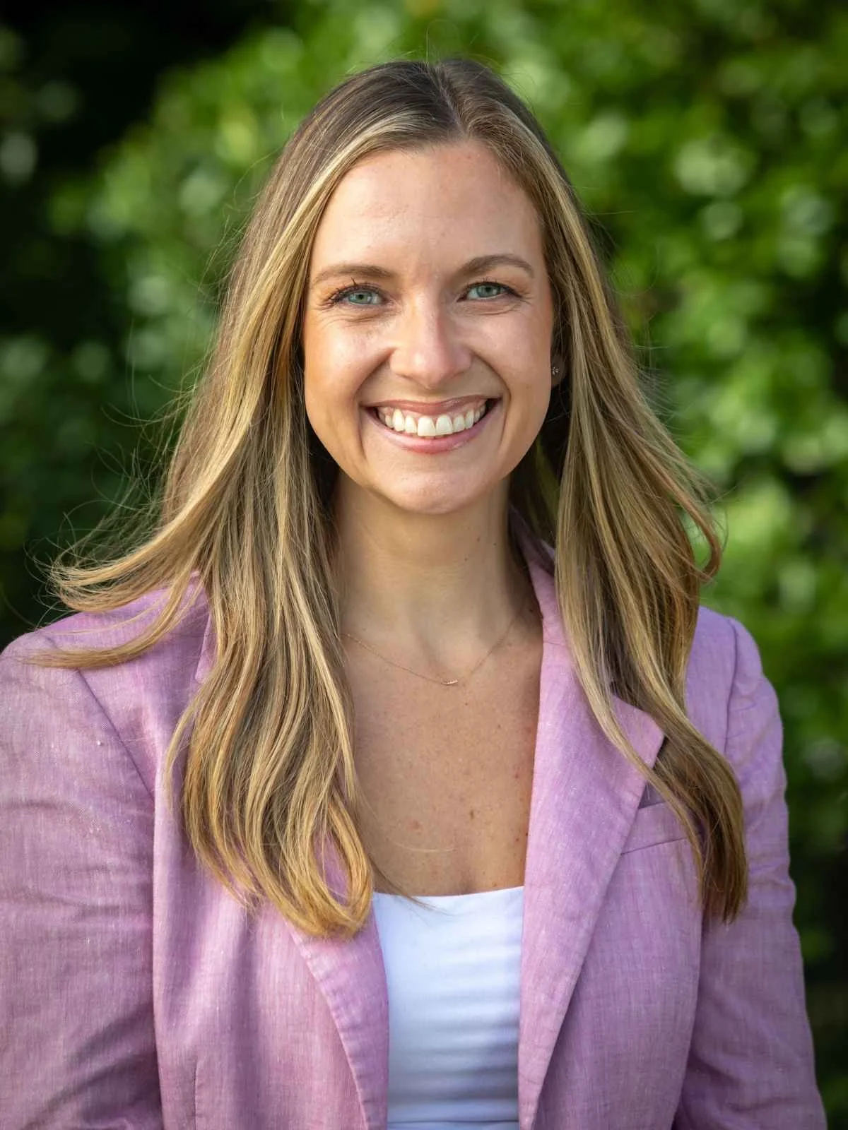 Portrait of Julia Maury, Dean of Students and Director of Admissions at Nantucket Lighthouse School, smiling outdoors in a pink blazer with greenery in the background.
