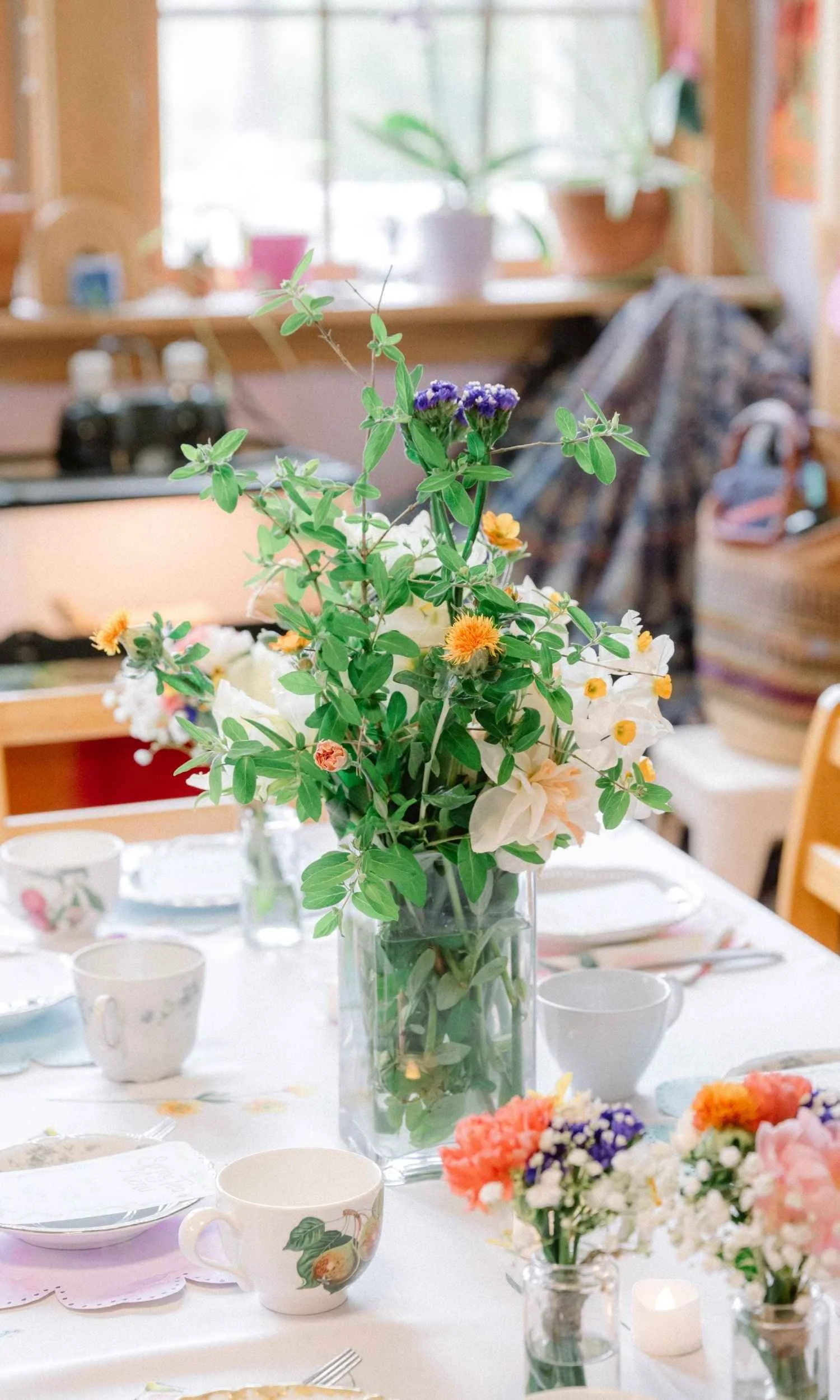 A beautifully arranged table for Nantucket Lighthouse School’s Small School Tea, featuring a colorful bouquet of flowers, teacups, plates, and small floral arrangements in a warm, welcoming classroom setting.