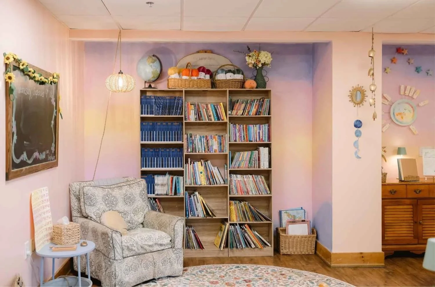 A cozy reading corner at Nantucket Lighthouse School featuring a patterned armchair, bookshelves filled with colorful books, a small table, and a chalkboard decorated with sunflowers, creating a warm and inviting classroom environment.