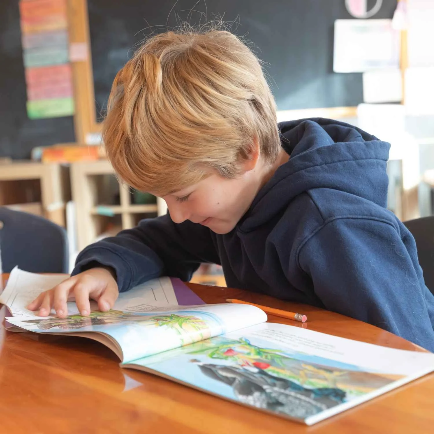 A Nantucket Lighthouse School Lower School student reads an open book at a wooden classroom table, focused on independent reading and learning in a quiet classroom setting.