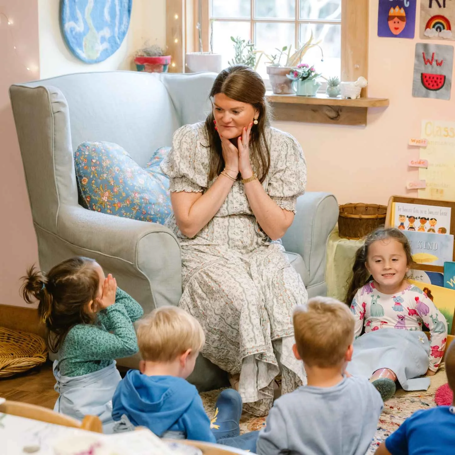 A Nantucket Lighthouse School Small School teacher leads a group activity with young students gathered on the floor in a welcoming classroom, surrounded by colorful artwork, plants, and natural materials.