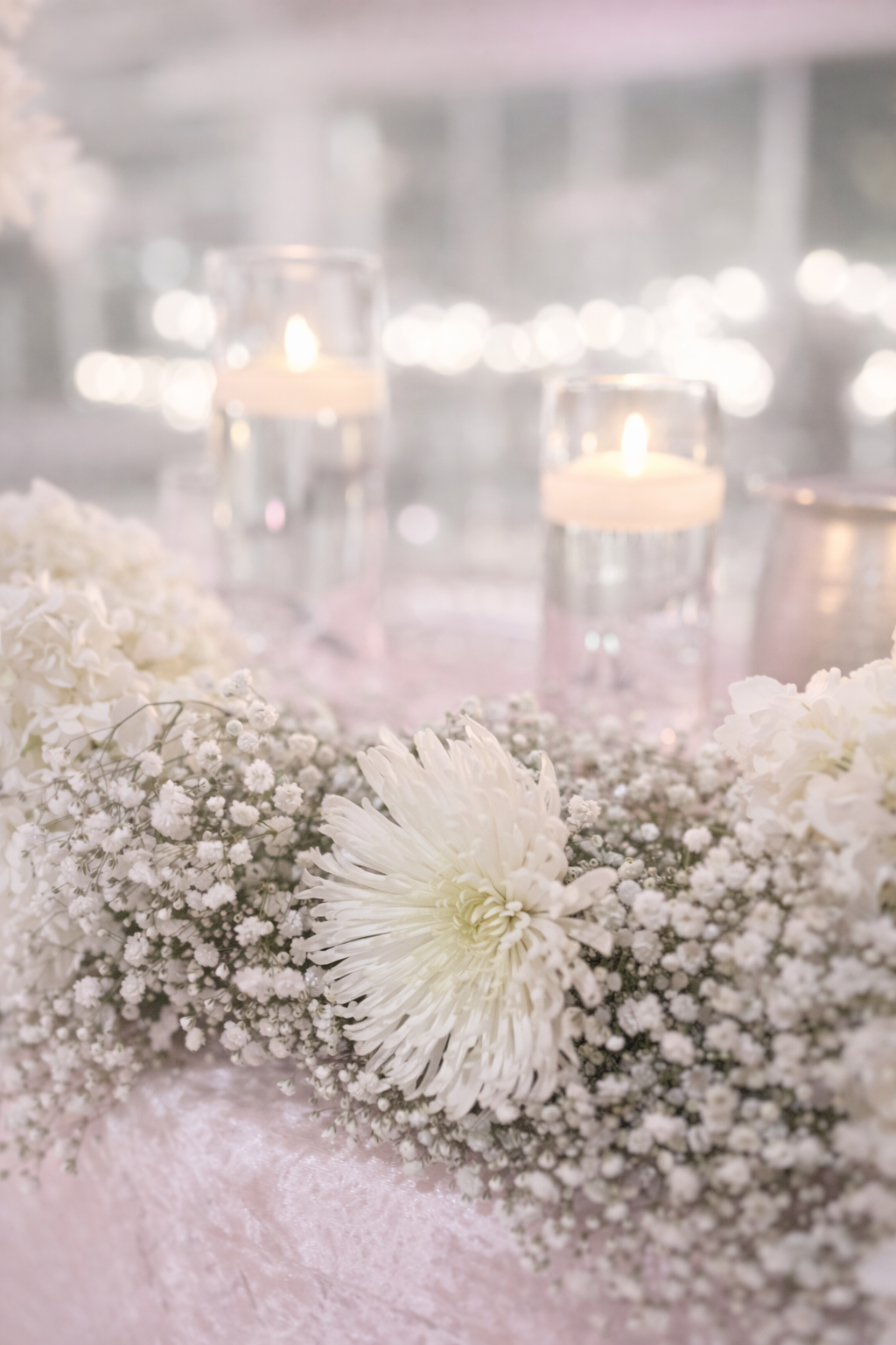 Elegant wedding table centerpiece with white flowers and lit candles.