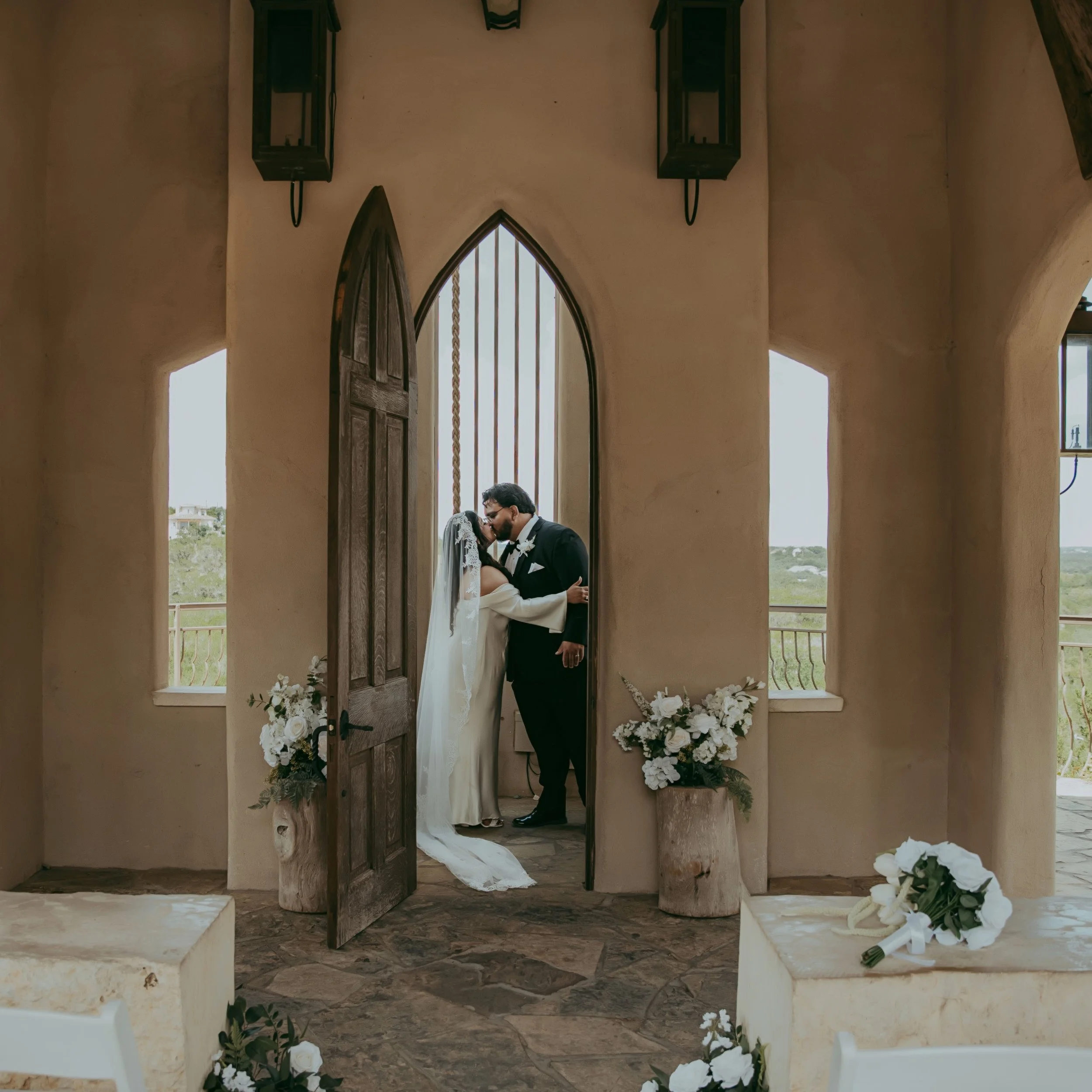 Couple kissing inside a church, surrounded by flower arrangements, during a wedding ceremony.