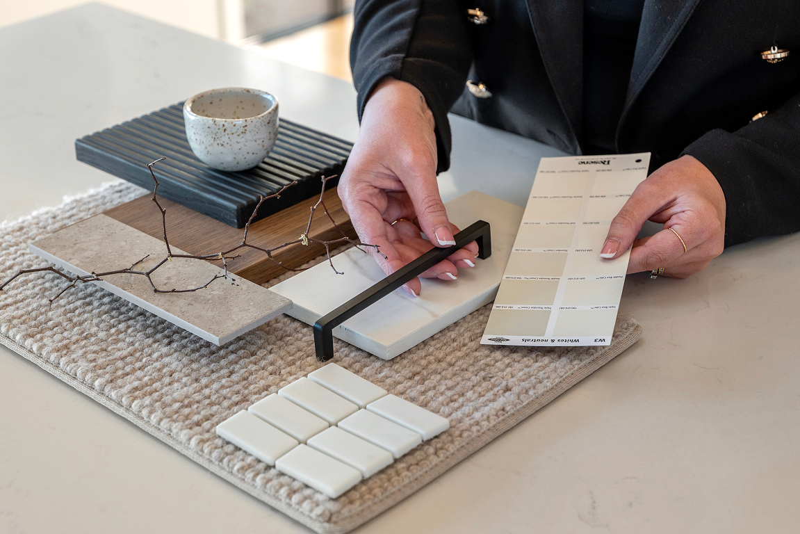 A person arranging tile samples on a table, with a cup, a stack of black tiles, and a color swatch nearby. Renovations, Extensions & Additional Dwellings Canterbury | Alterhouse