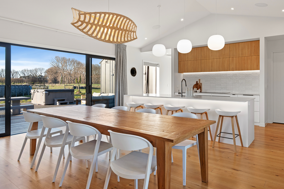Modern open-concept kitchen and dining area with wooden dining table, white chairs, pendant and globe lights, large sliding glass doors, and a view of an outdoor patio and backyard. Renovations, Extensions & Additional Dwellings Canterbury | Alterhou