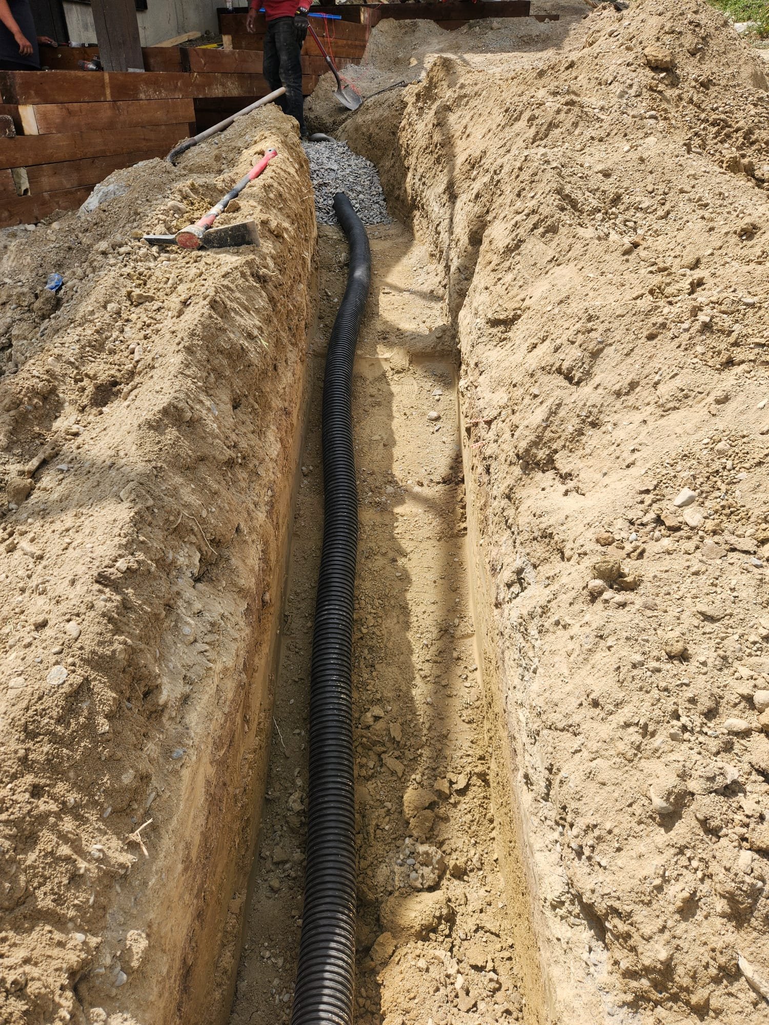 Construction worker laying black corrugated pipe in a long trench with dirt walls for underground utility installation.